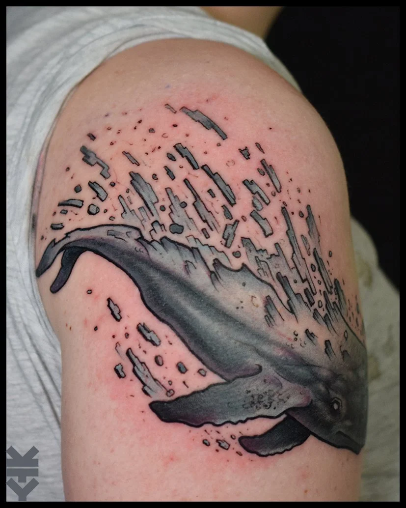 Tattoo of a whale with pixelated effects on upper arm.