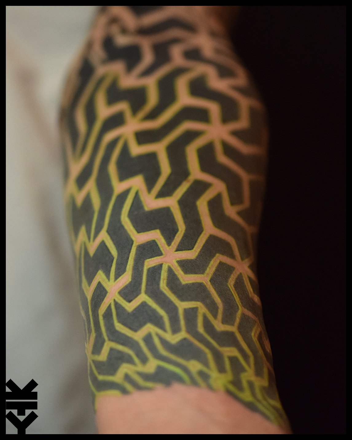 A tattoo on a person's arm featuring a black and yellow geometric maze-like pattern.