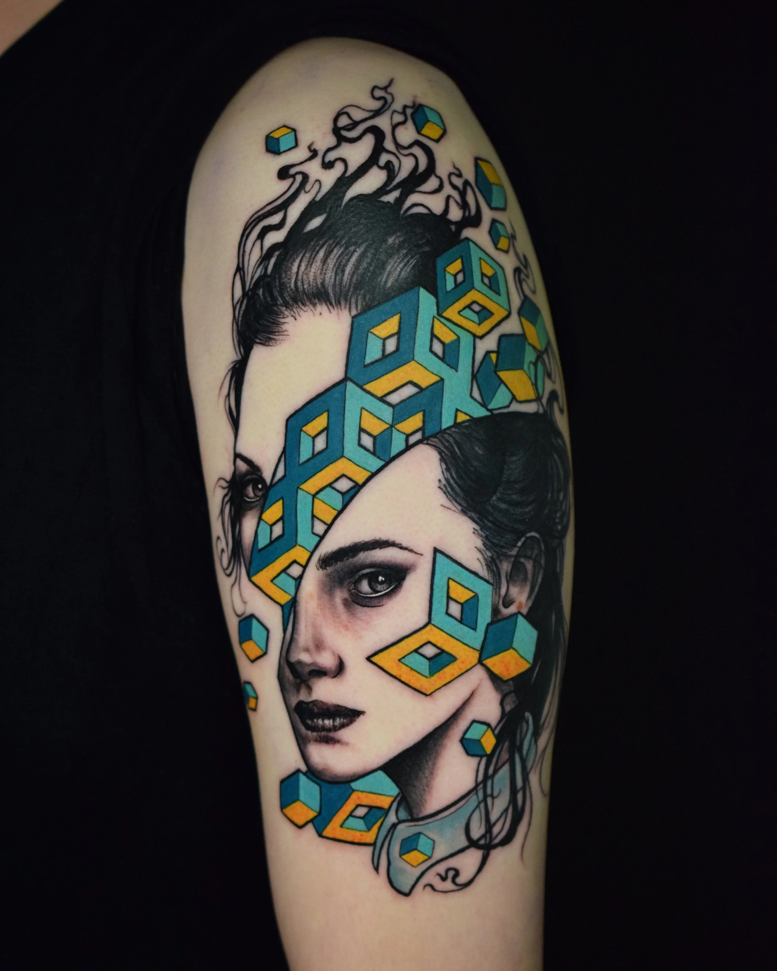 Tattoo of two realistic women's faces interwoven with colorful 3D cube designs on a person's arm.