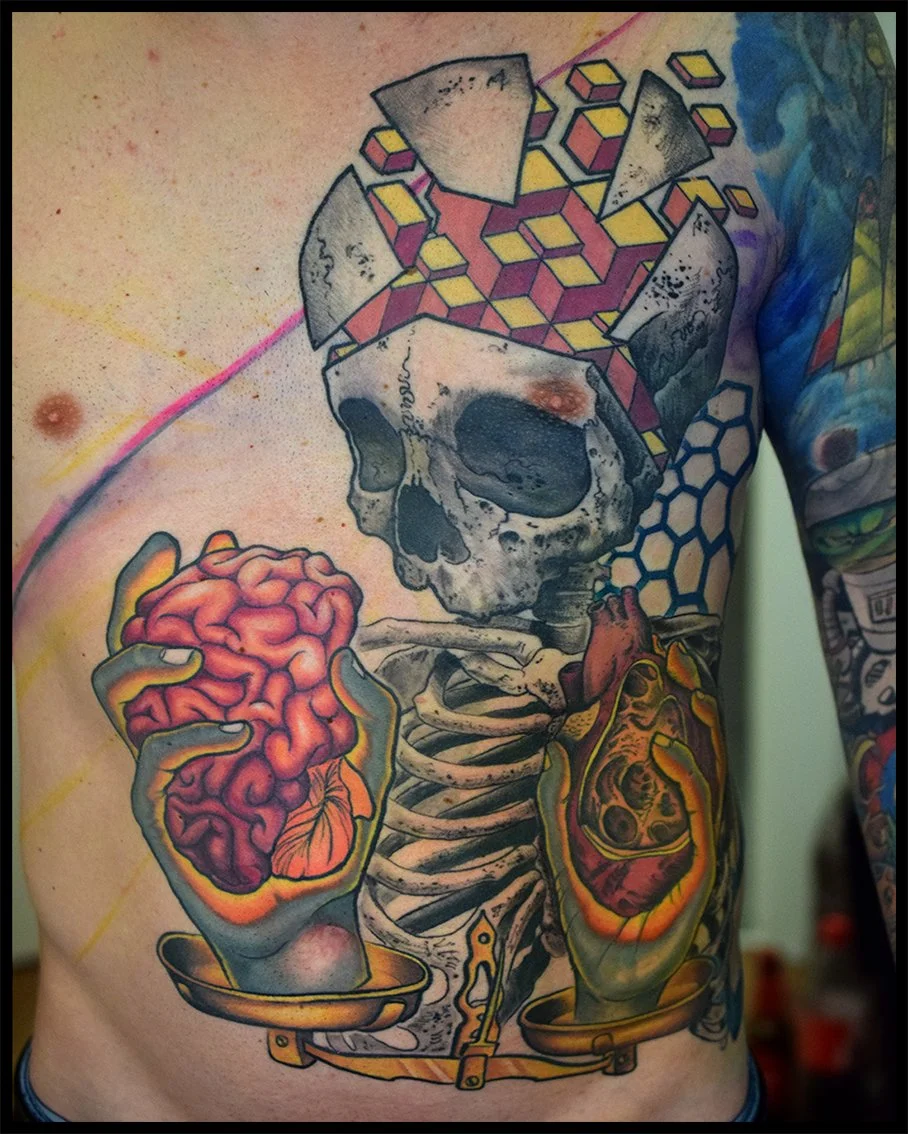 A colorful tattoo featuring a skull with a geometric pattern and cube design on its head. The skull holds a pink brain in one hand and a realistic human heart in the other, with both resting on trays.