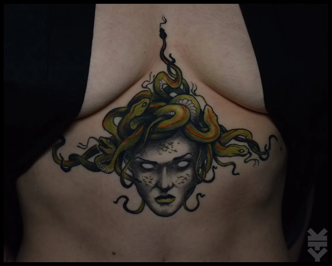 Tattoo of Medusa with snakes on her head, featuring black, yellow, and orange colors, on a person's chest.