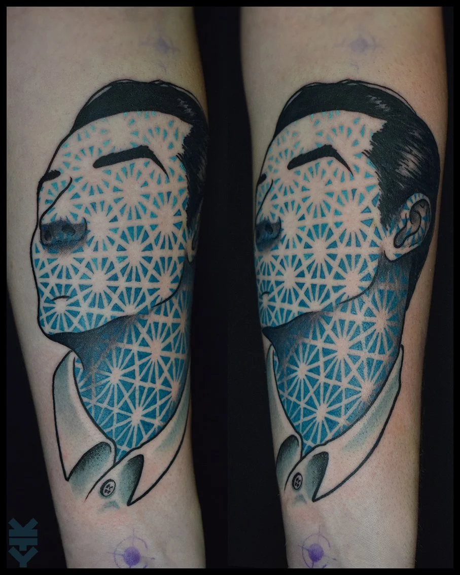 Tattoo of a stylized, black and white portrait of a woman's face with her eyes closed, overlaid with a pattern of blue geometric starburst shapes, on a person's arm.