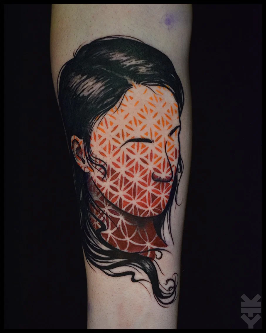 Tattoo of a woman's face with black hair, featuring geometric orange and white patterns covering the face and neck.