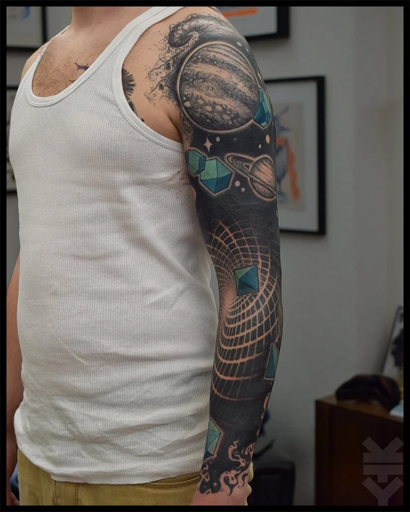 Tattoo sleeve featuring space-themed designs including planets, stars, a grid pattern, and geometrical shapes on a person's arm.