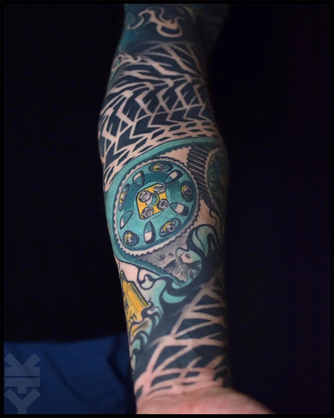 Tattooed arm with geometric and mechanical designs, including gears and intricate patterns.