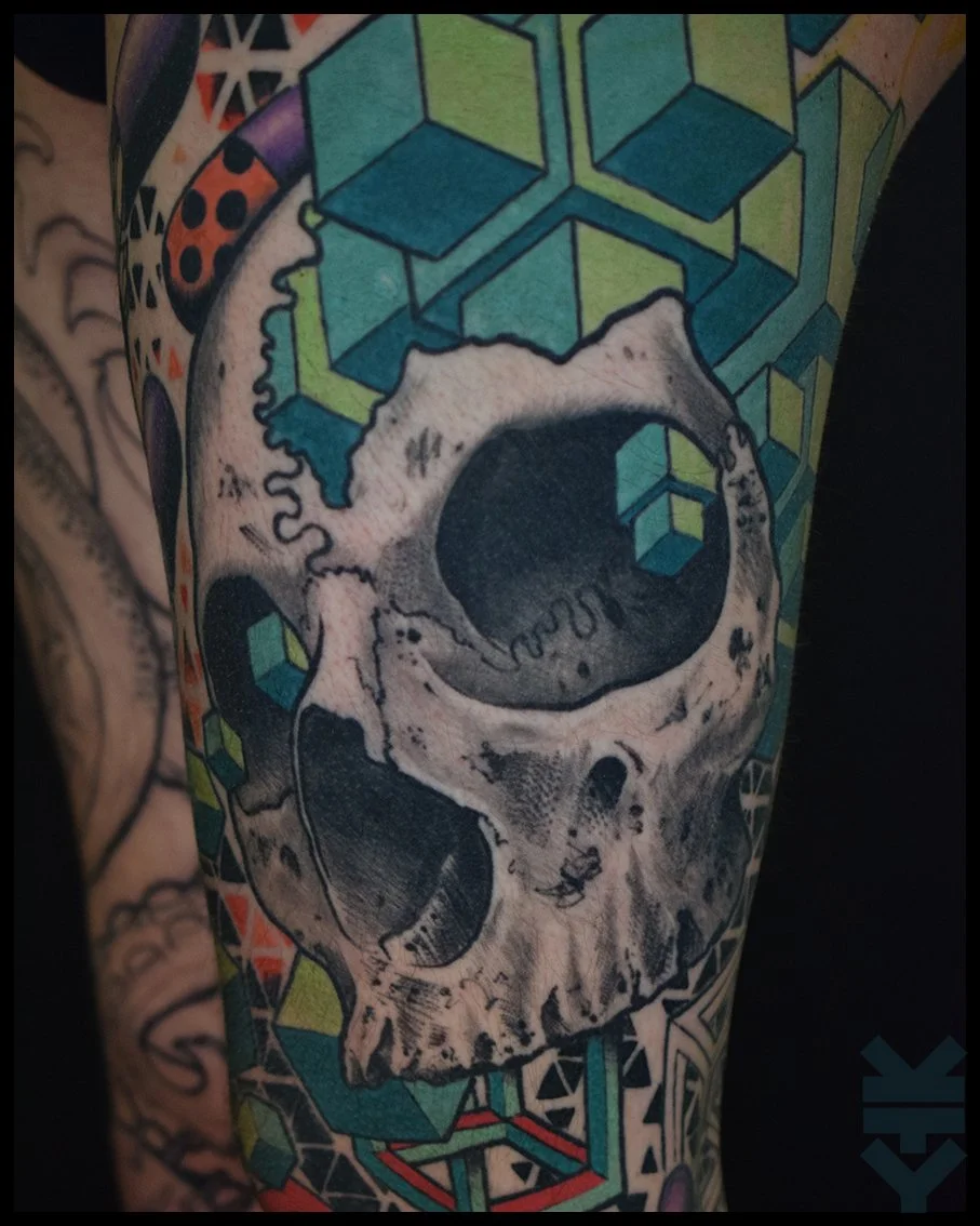 Tattoo of a skull with geometric patterns and cubes in shades of green, blue, and black.