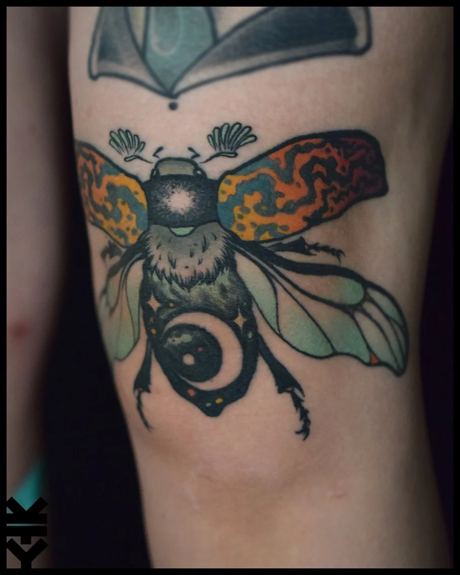 Tattoo of a bee with colorful wings on person's arm.