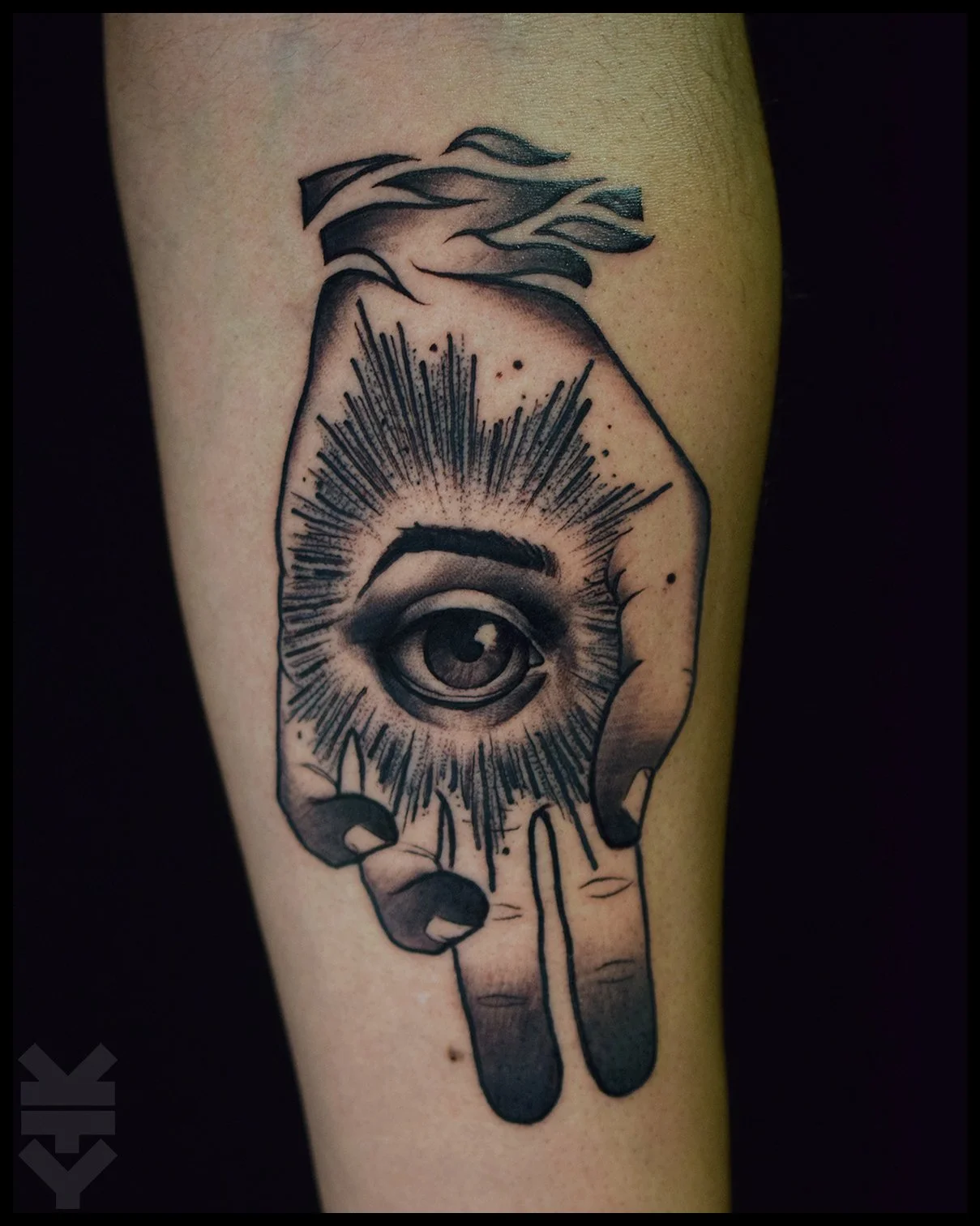 A black and gray tattoo of a hand with an eye in the palm, surrounded by radiating lines and dripping ink, on a person's arm.