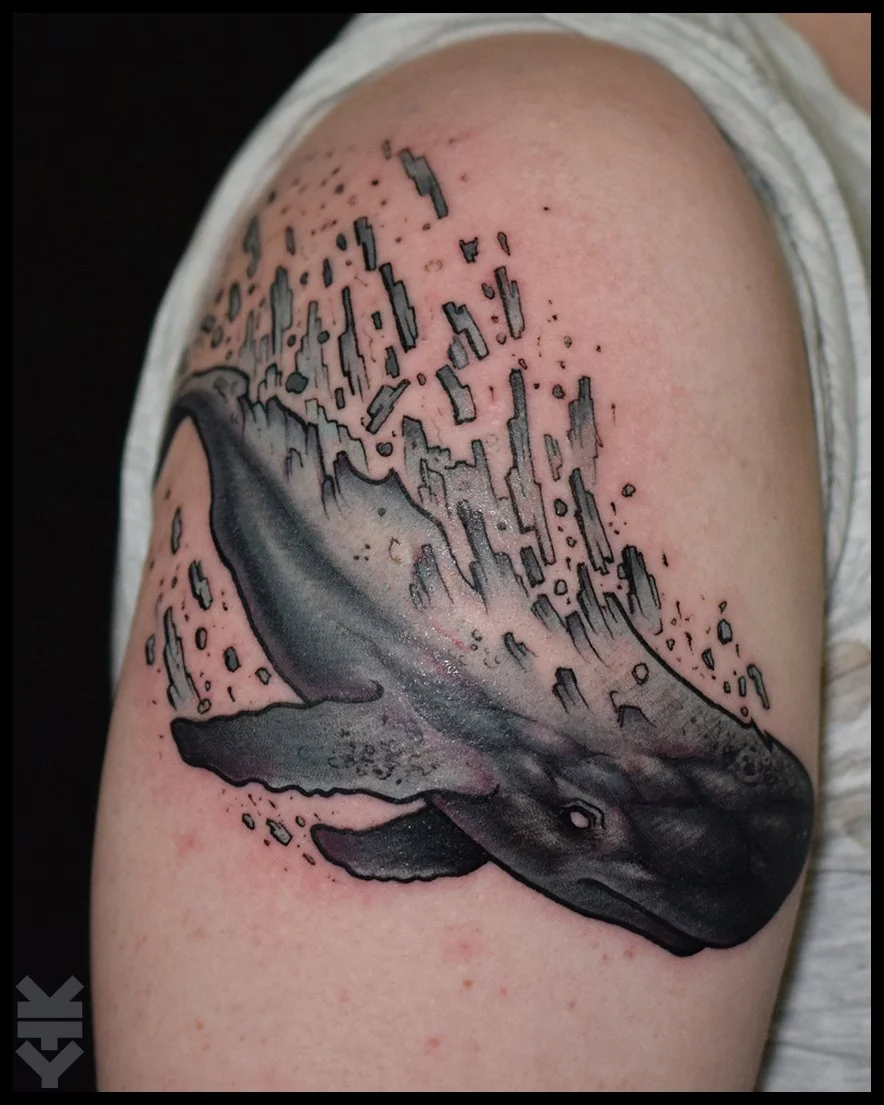 Tattoo of a whale, depicted in black and gray, with abstract geometric shapes above it on a person's upper arm