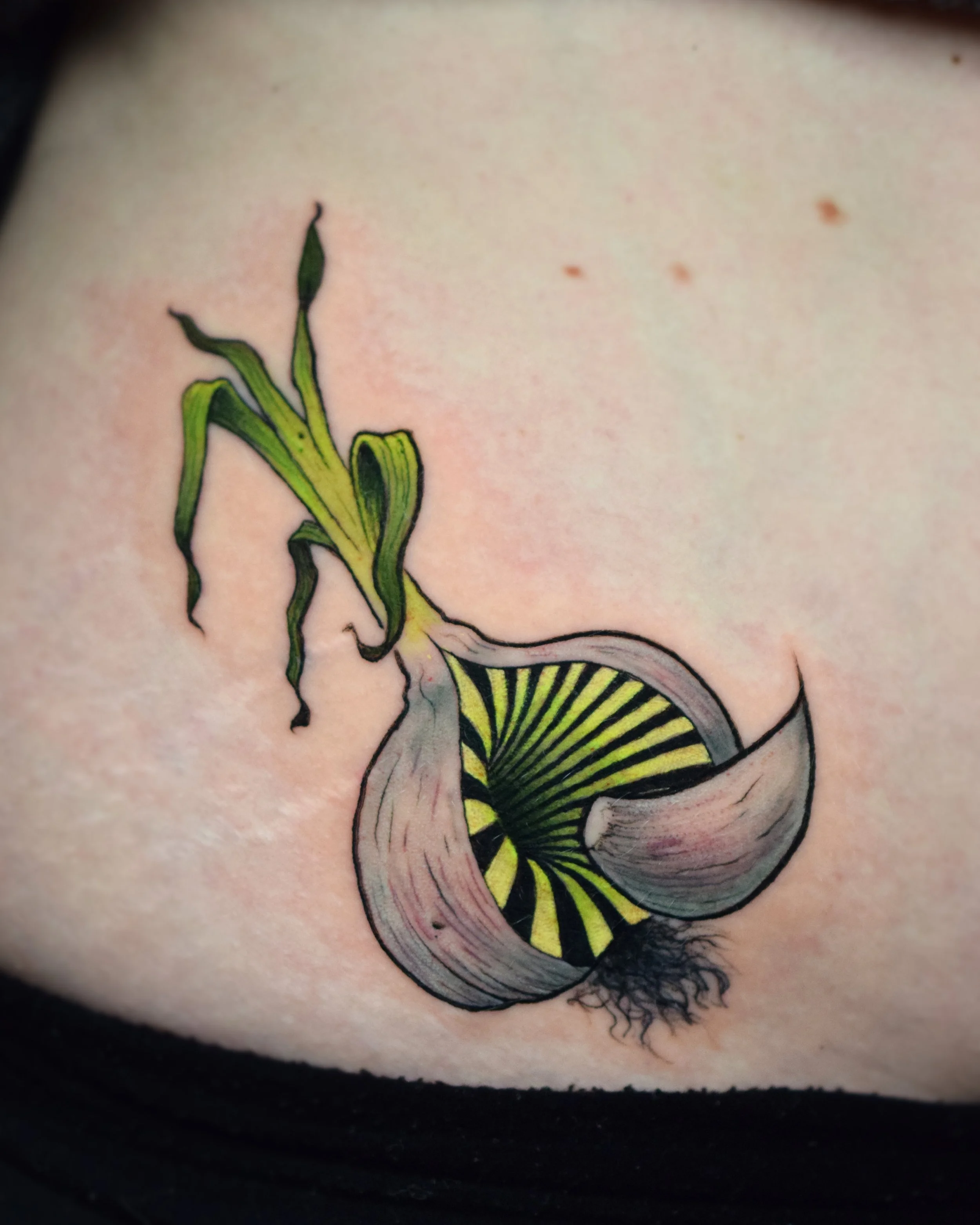 Tattoo of a green and black spiral creature with roots and green tentacle-like appendages on skin.
