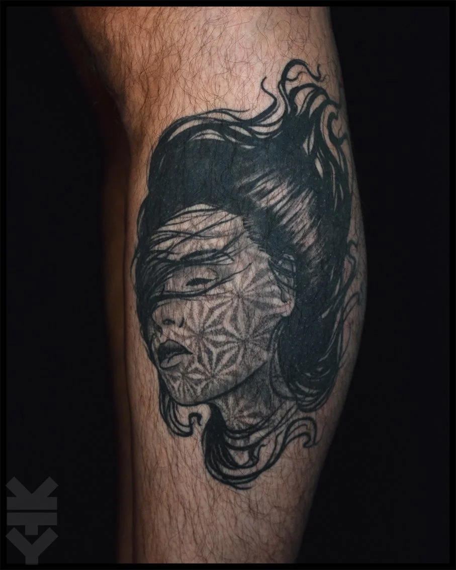 Tattoo of a woman's face with closed eyes and flowing hair, overlaid with a geometric pattern, on a person's arm.