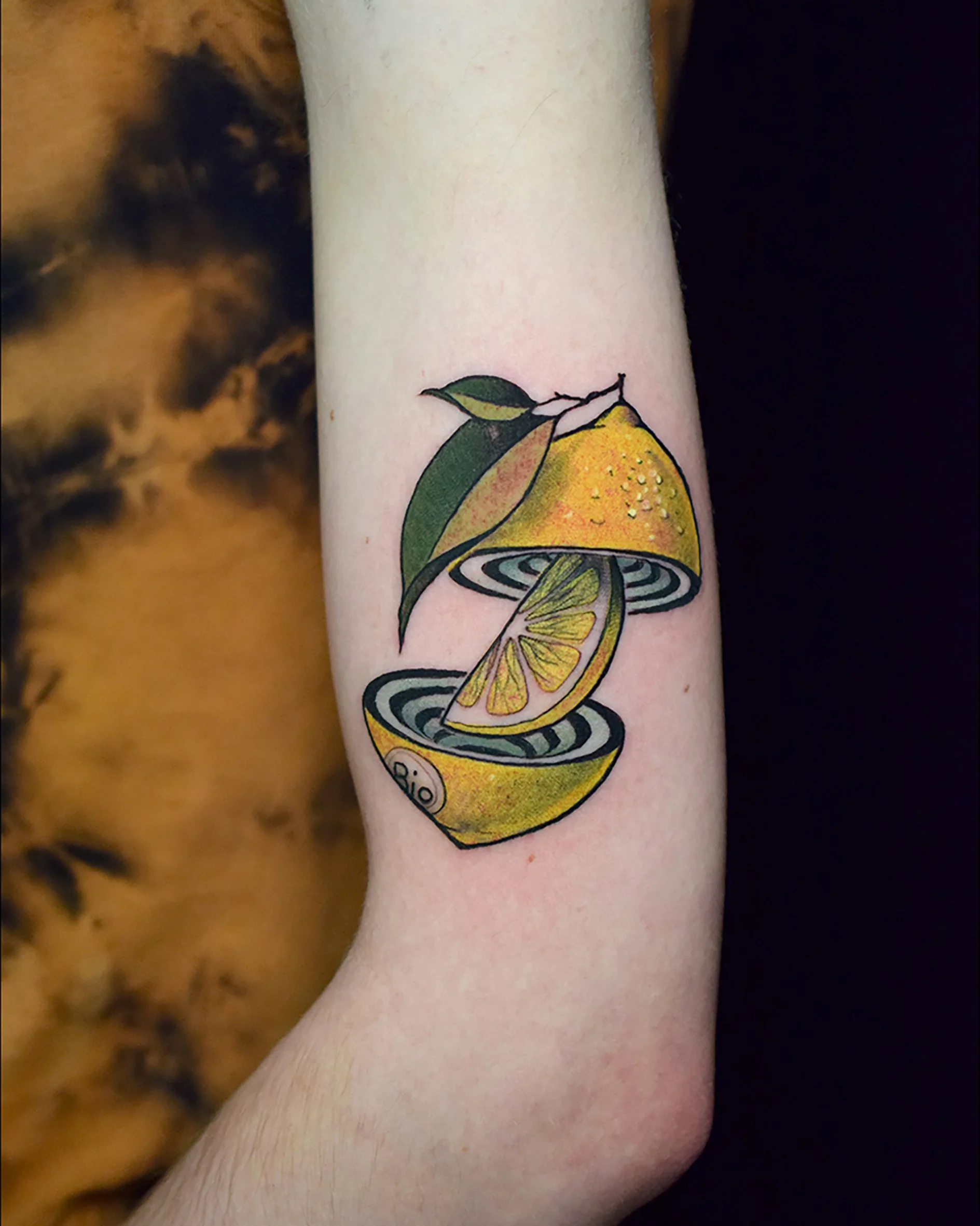 Tattoo of a lemon that is sliced and peeled, with a leaf attached at the top.