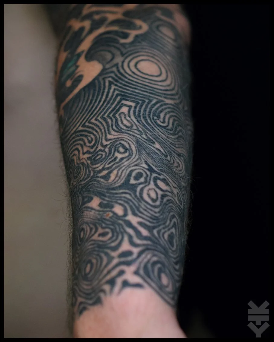Detailed black and gray tattoo sleeve with abstract, concentric and swirling patterns on a person's arm.