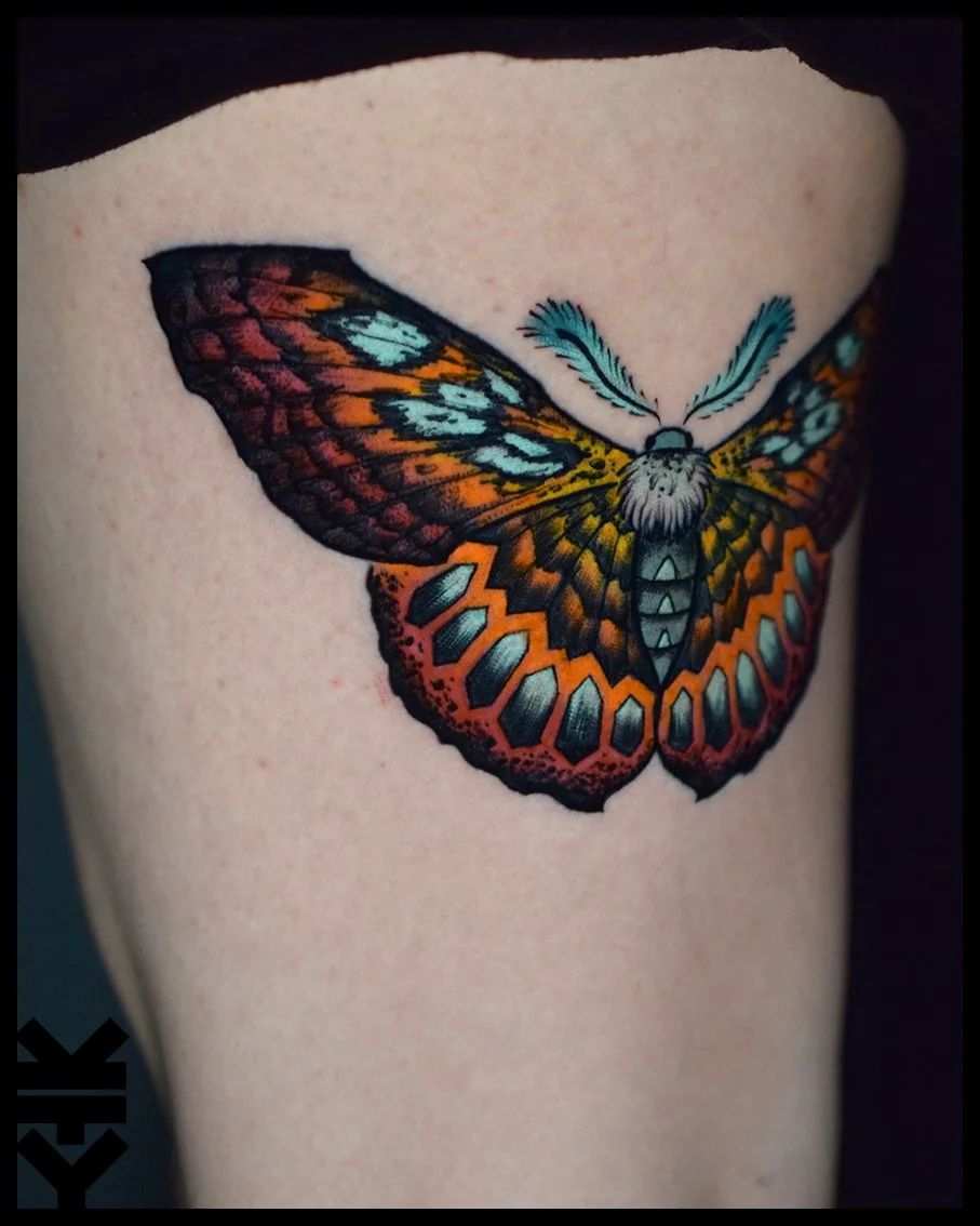 Colorful butterfly tattoo on skin with orange, black, blue, and yellow details.