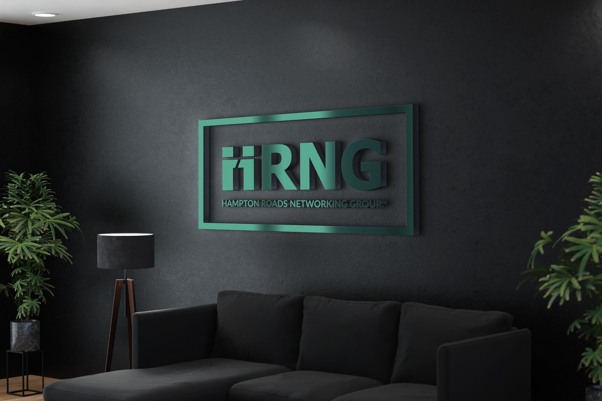 Modern office lounge with black sofa, large green potted plants, a black floor lamp, and a wall sign reading 'HRNG Hampton Roads Networking Group' in a sleek interior design.
