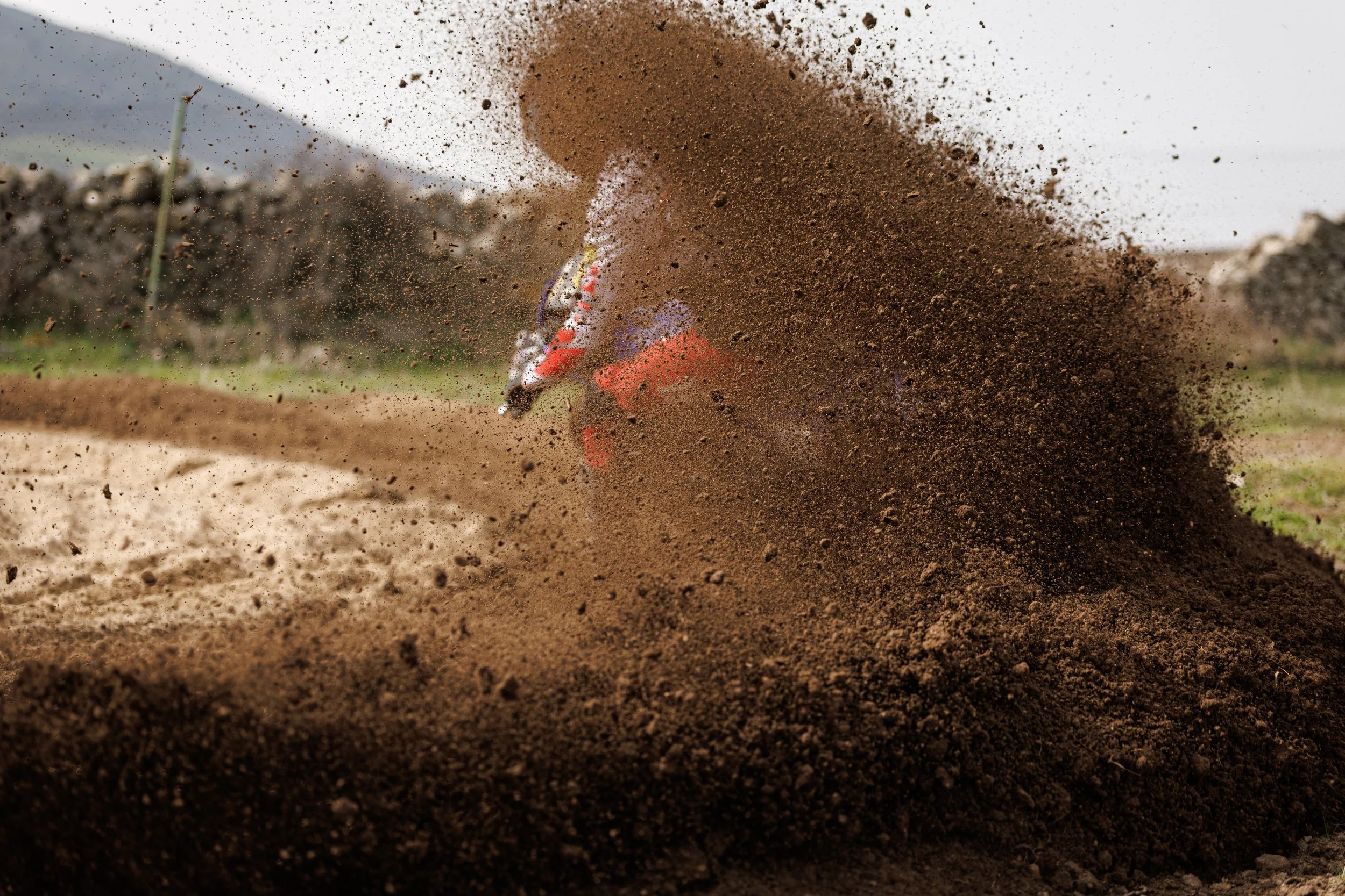 Moto de dirt bike haciendo un salto que levanta tierra en un circuito al aire.