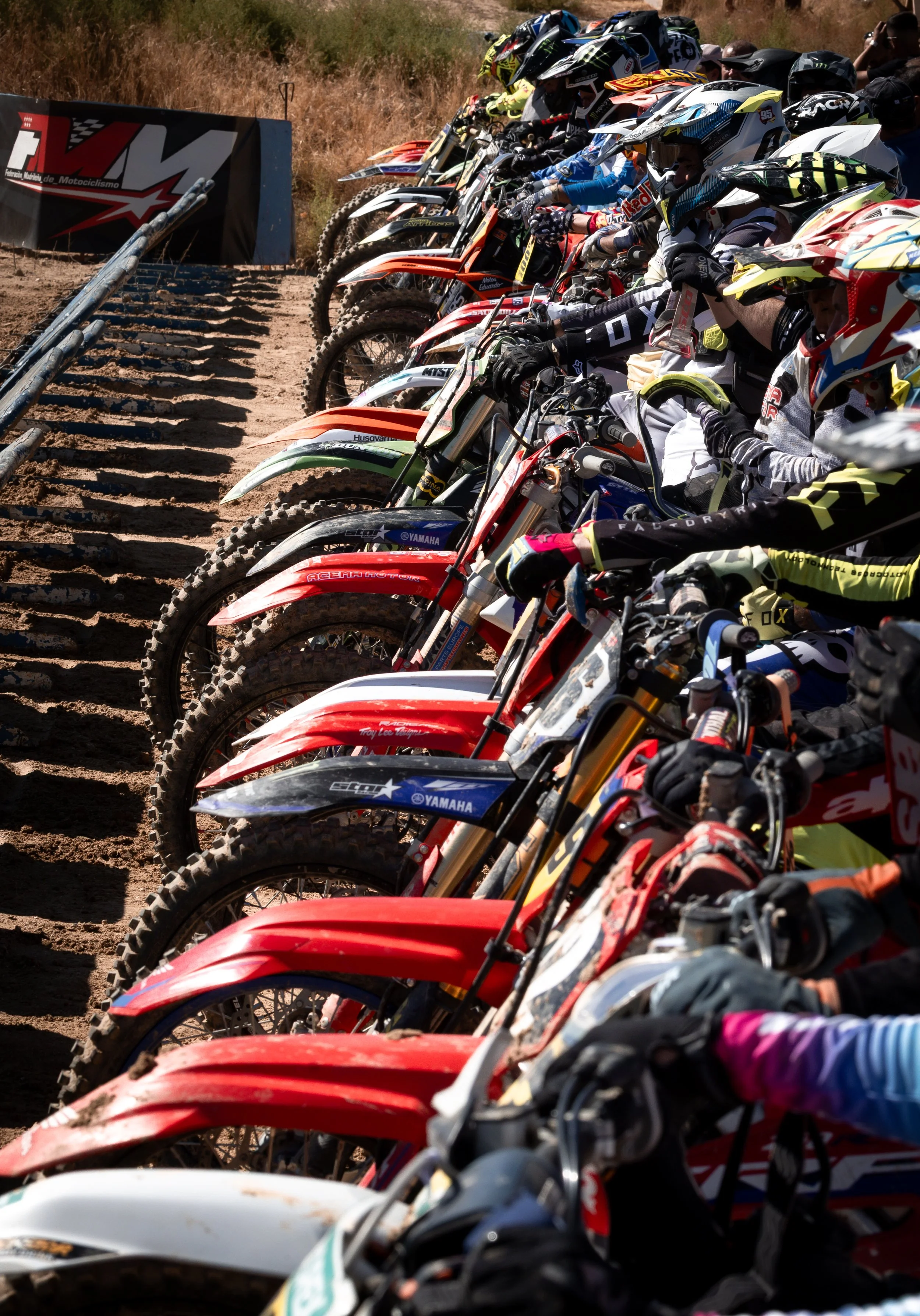 Varias motocicletas de dirt bike alineadas en una línea en un campo, con pilotos preparados para una competencia de motocross.