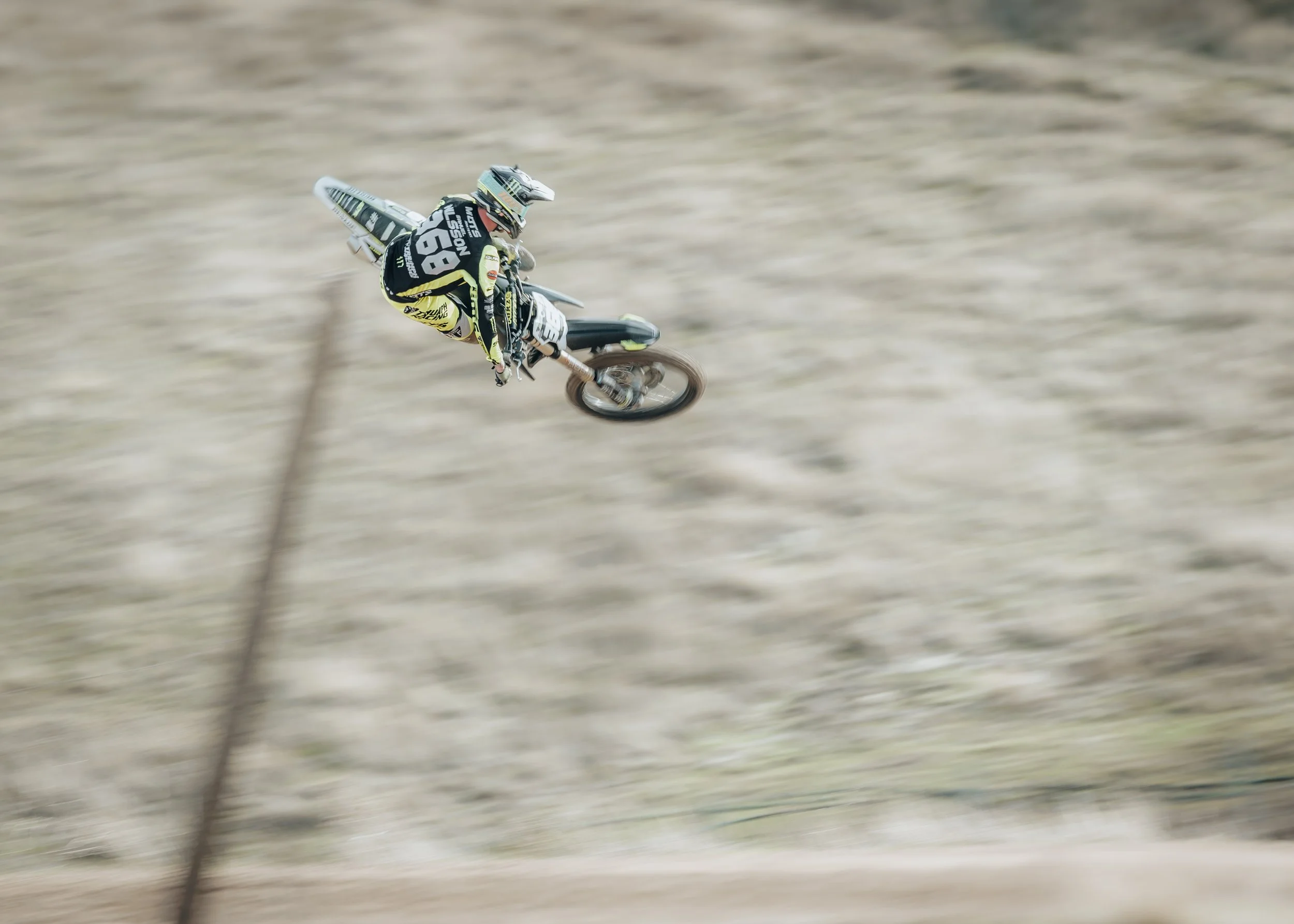 Un piloto de motocross en el aire durante una competencia en un campo árido.