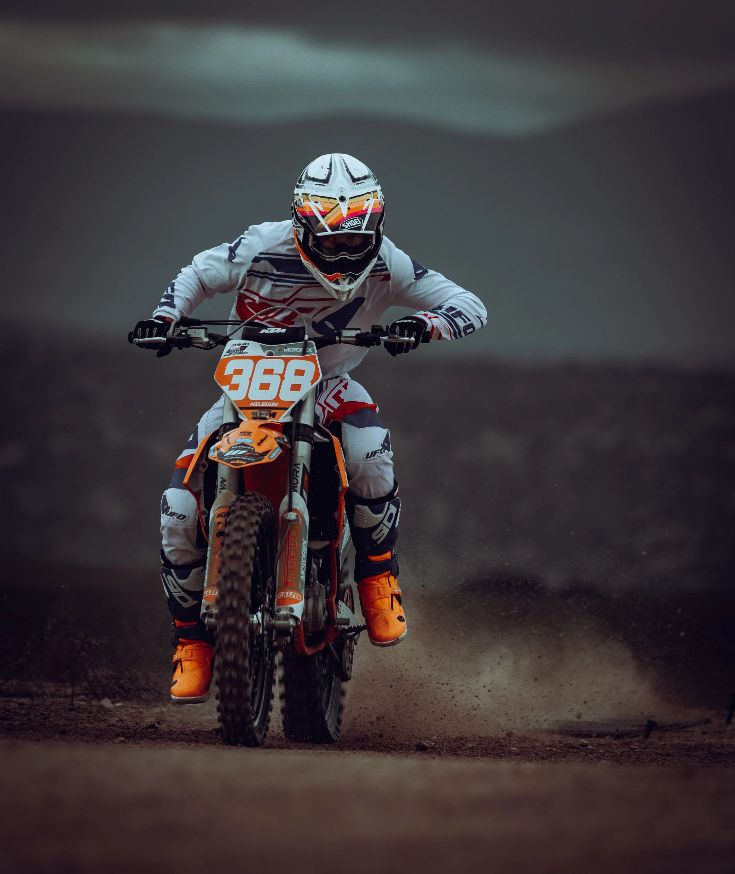Piloto de motocross en la pista, usando casco, vestimenta de protección blanca y naranja, y motocross naranja.