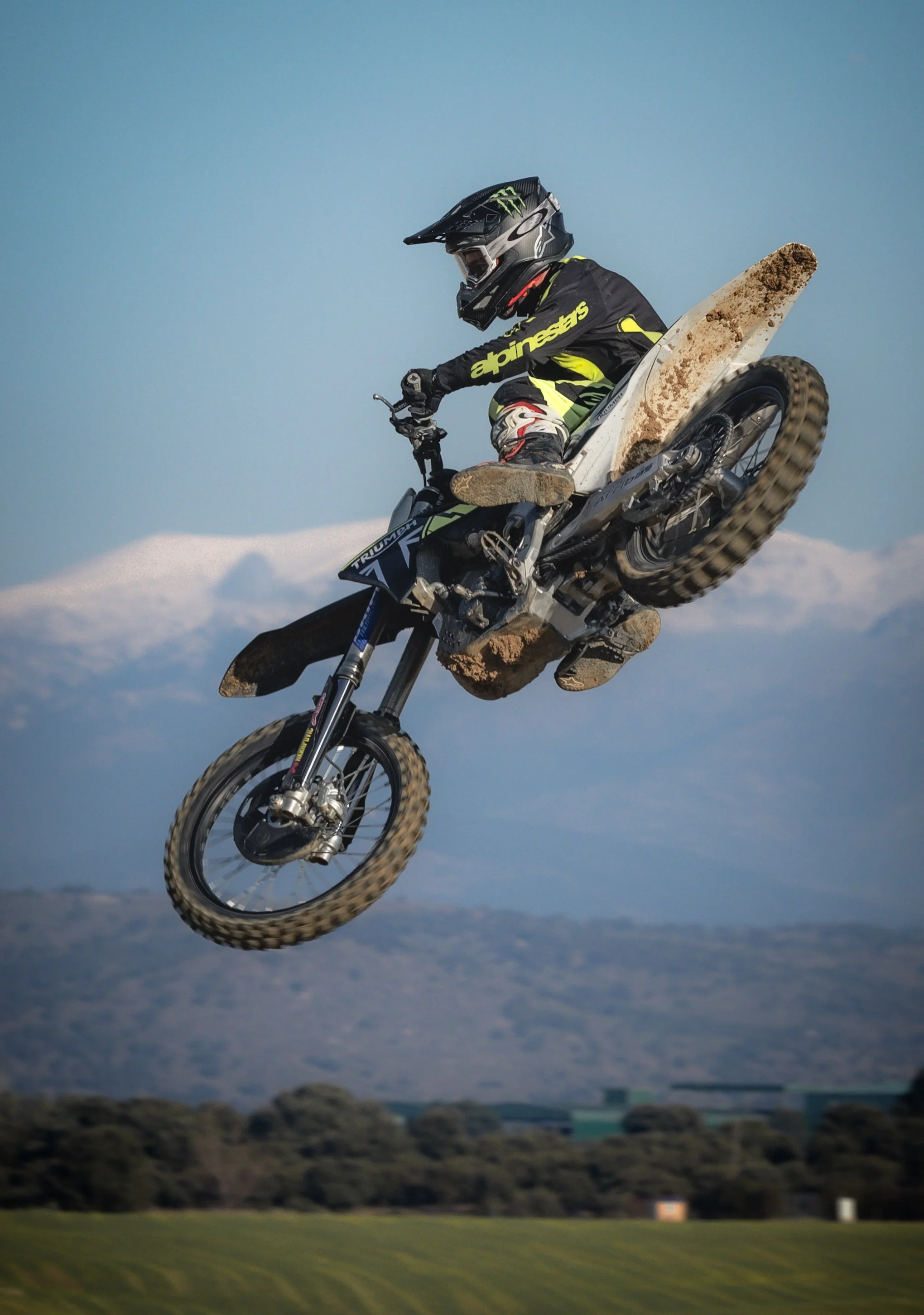 Un motociclista realizando un salto en un deporte extremo con fondo de montañas y cielo despejado.