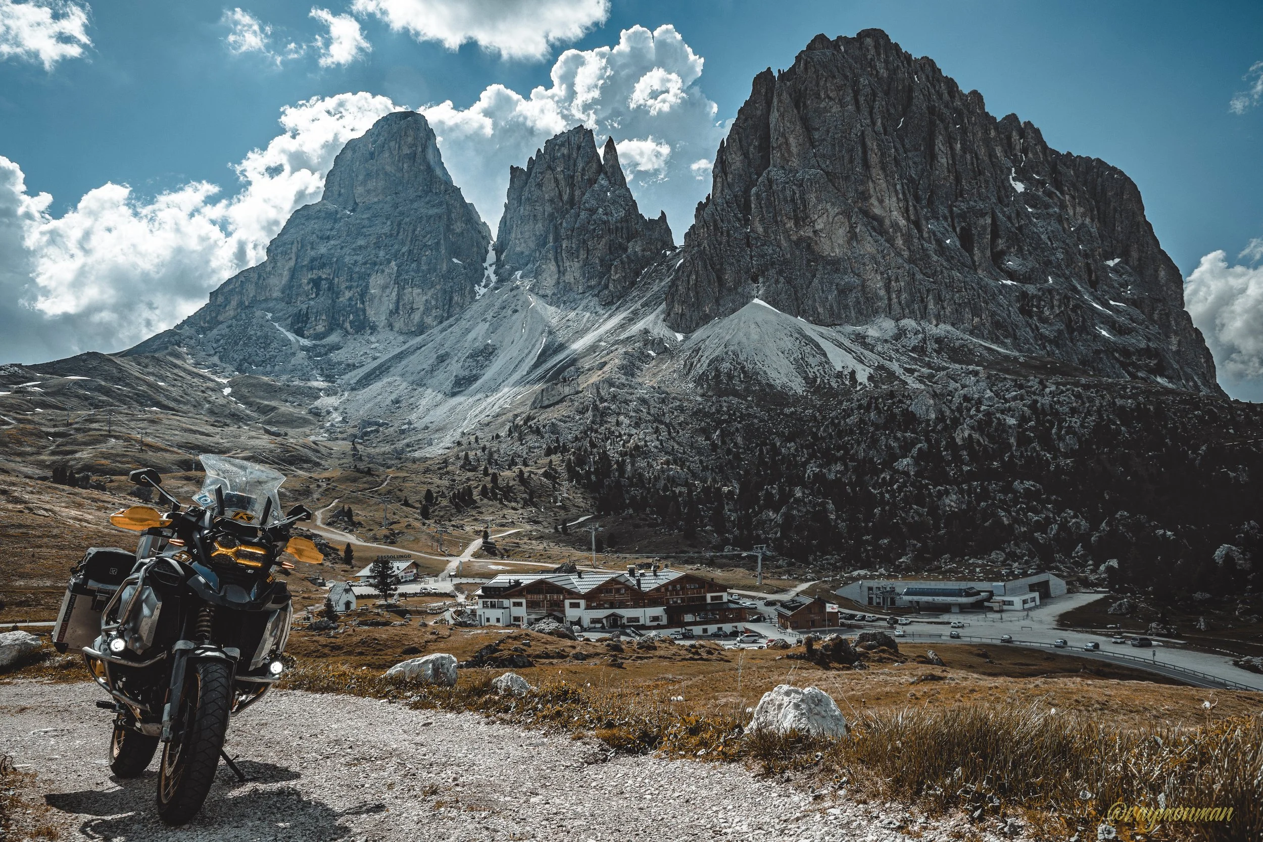 Motocicleta en primer plano con montañas y pueblo al fondo en un paisaje de montaña.