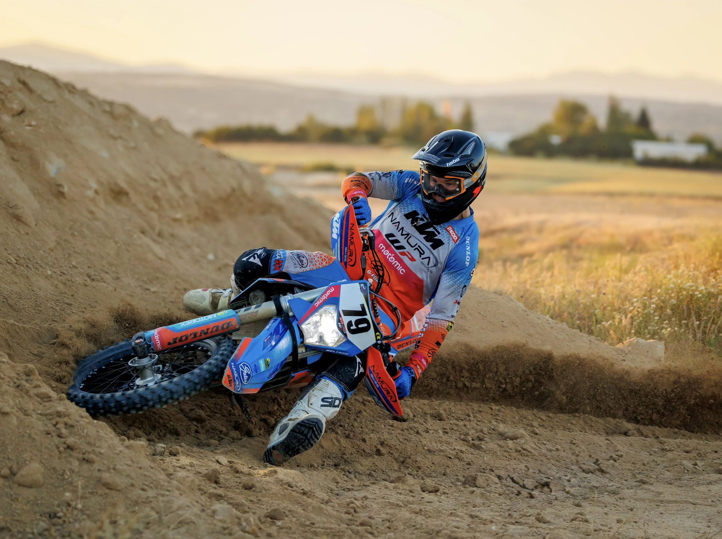 Motociclista en acción tomando una curva en una pista de tierra en un día soleado.