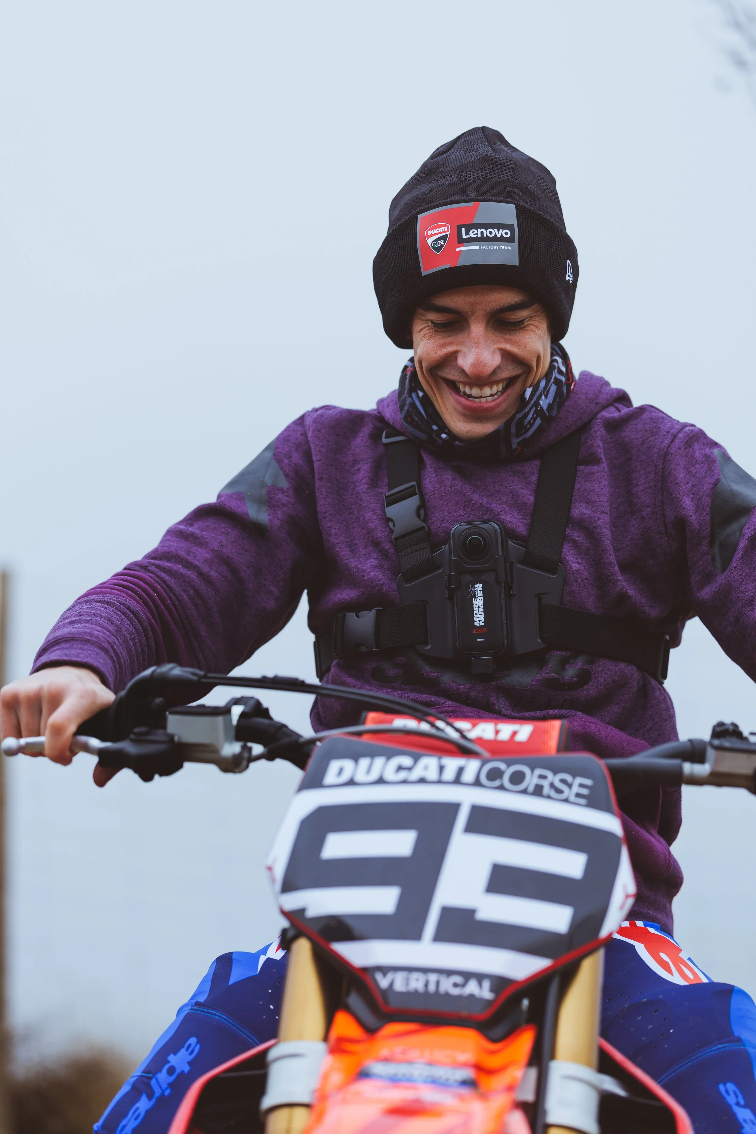 Joven sonriente montando una moto de dirt bike, con protecciones y ropa de motocross, en un día nublado.