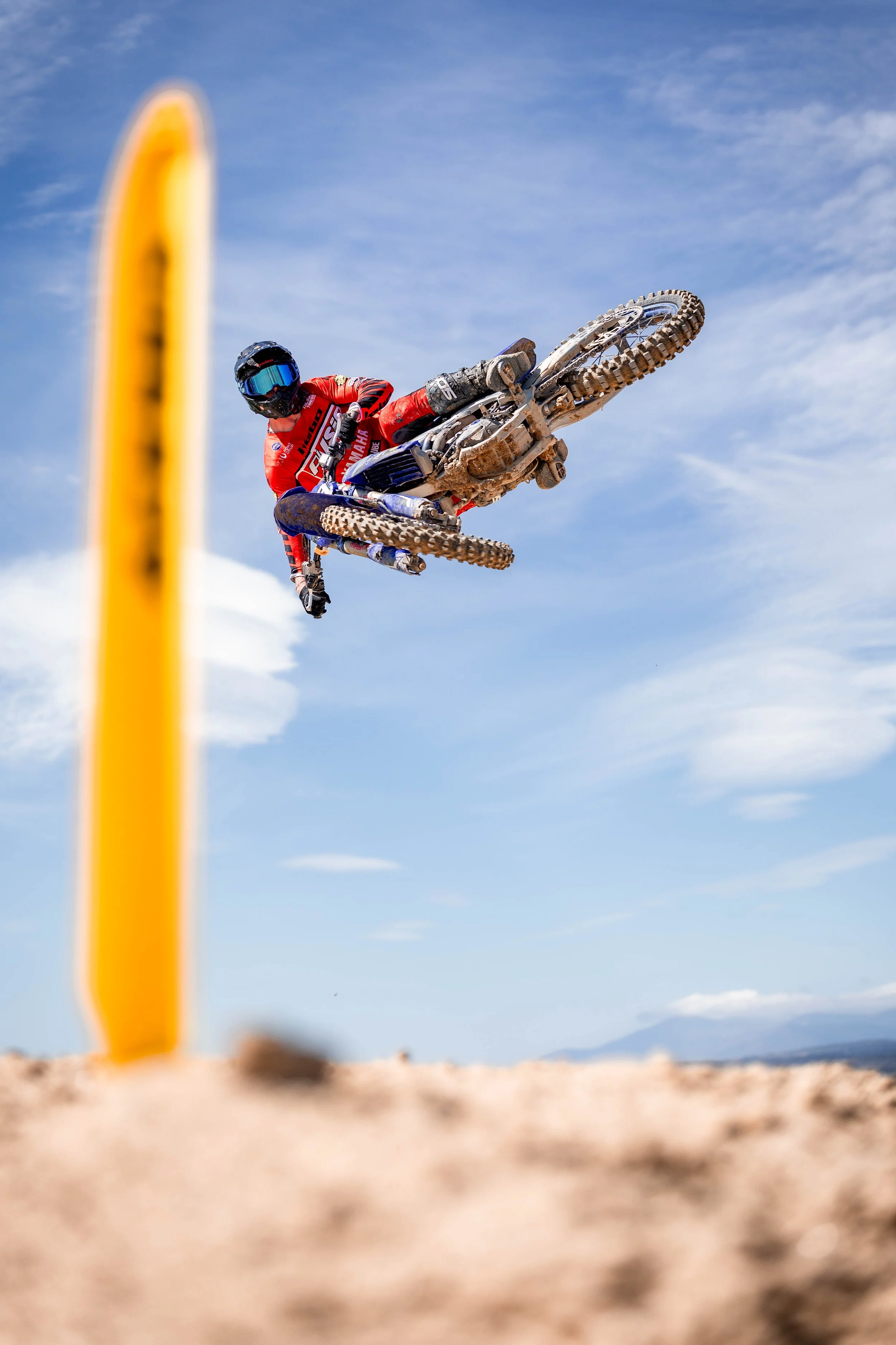 Un motociclista realizando un salto en una pista de arena, con un cielo despejado y algunas montañas al fondo. espectacular
