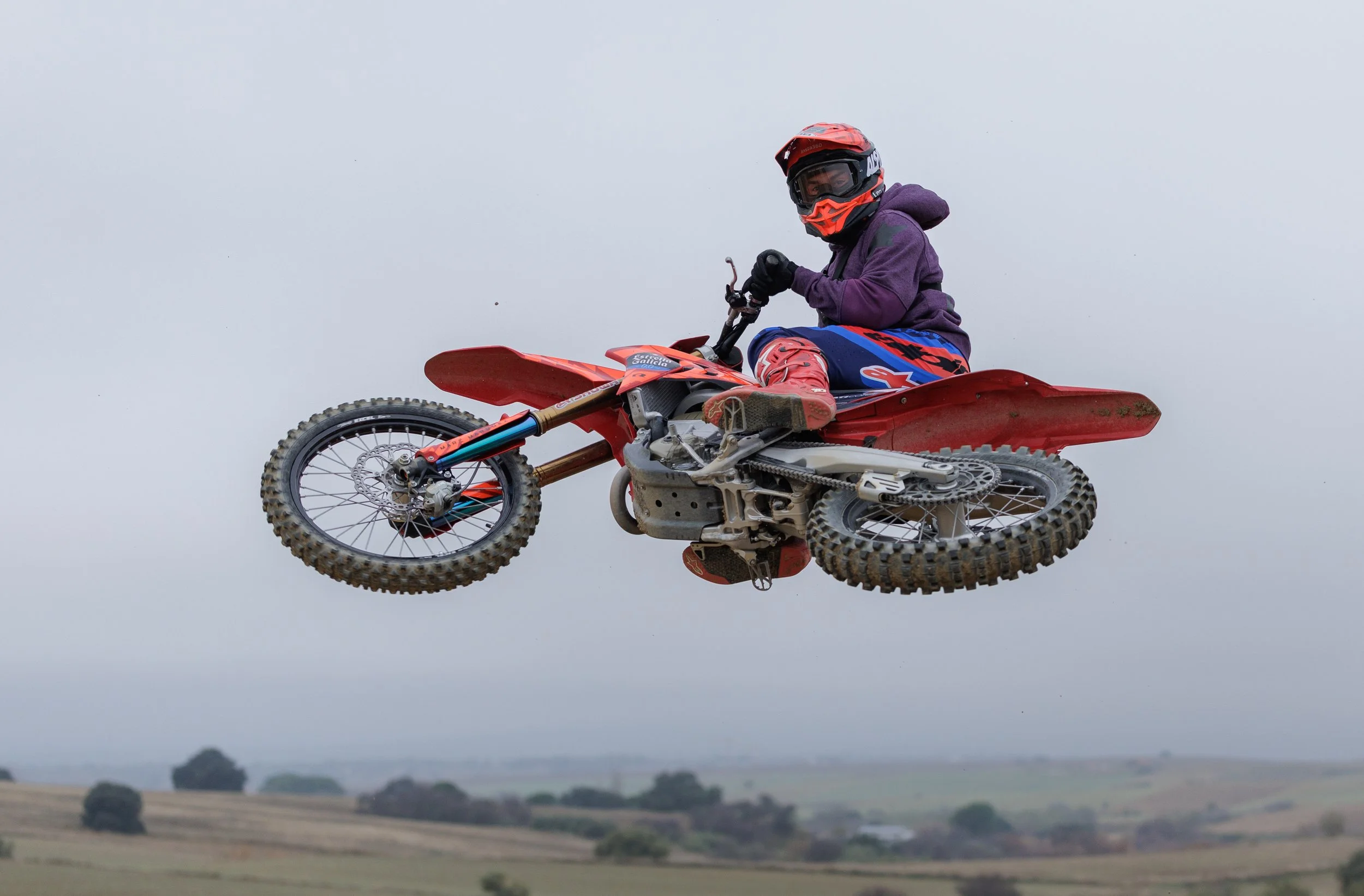 Una persona en una moto de motocross en el aire durante un salto en un día nublado.