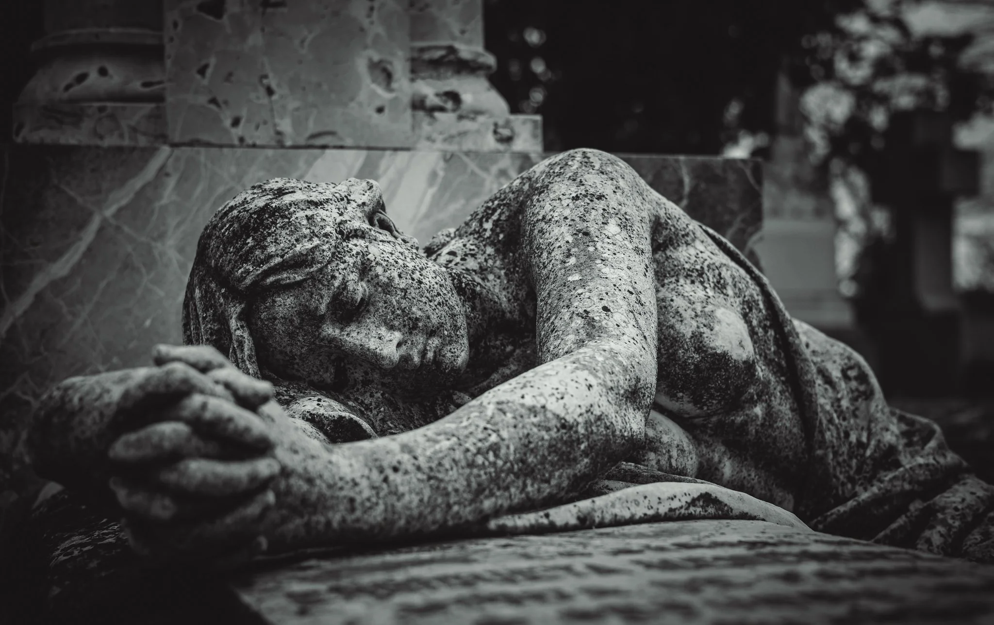 Estatua de una mujer durmiendo, hecha de piedra, en un entorno exterior.