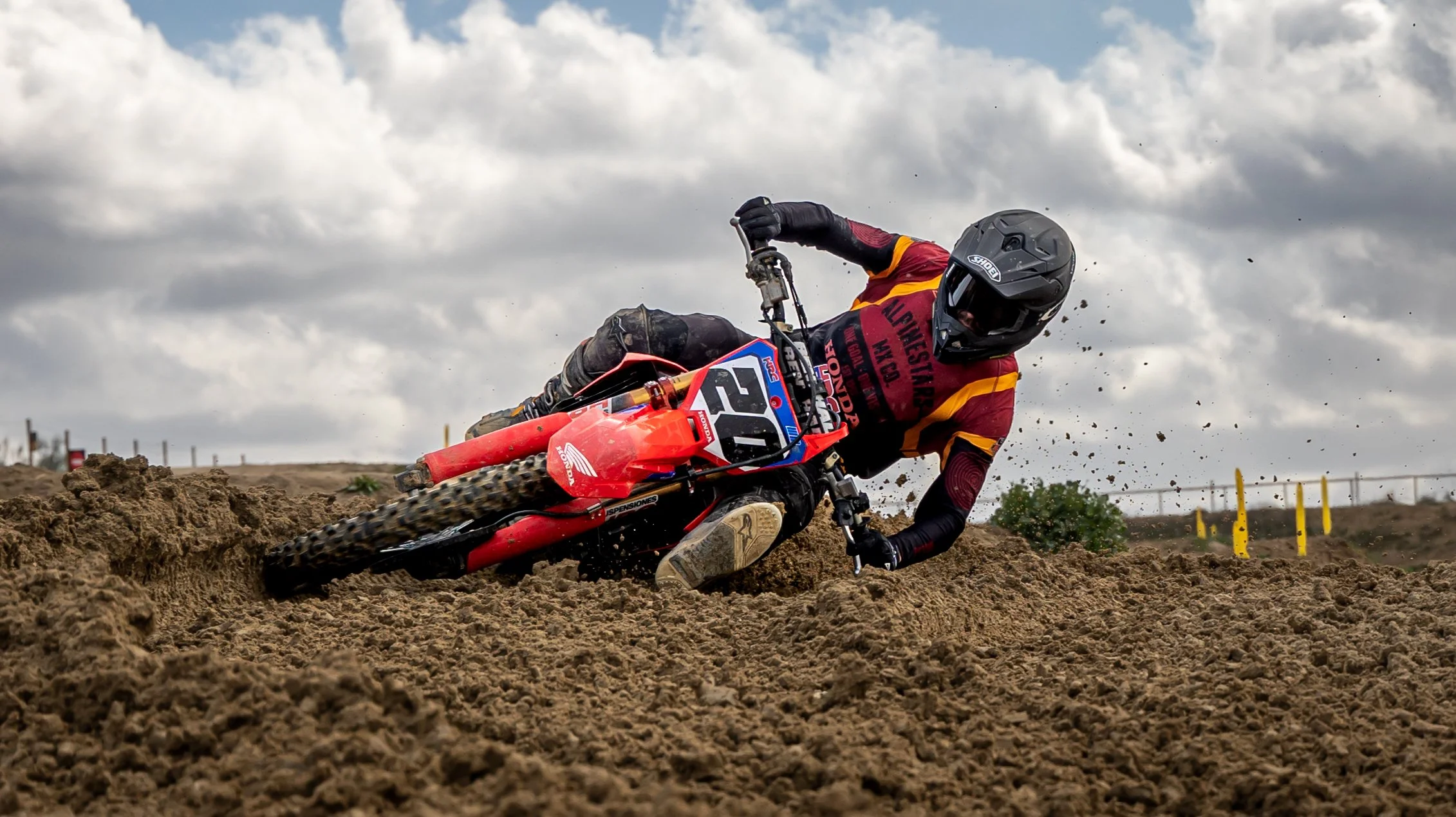 Motociclista en una pista de tierra, inclinado hacia un lado mientras toma una curva en una carrera con cielo nublado. Motocross