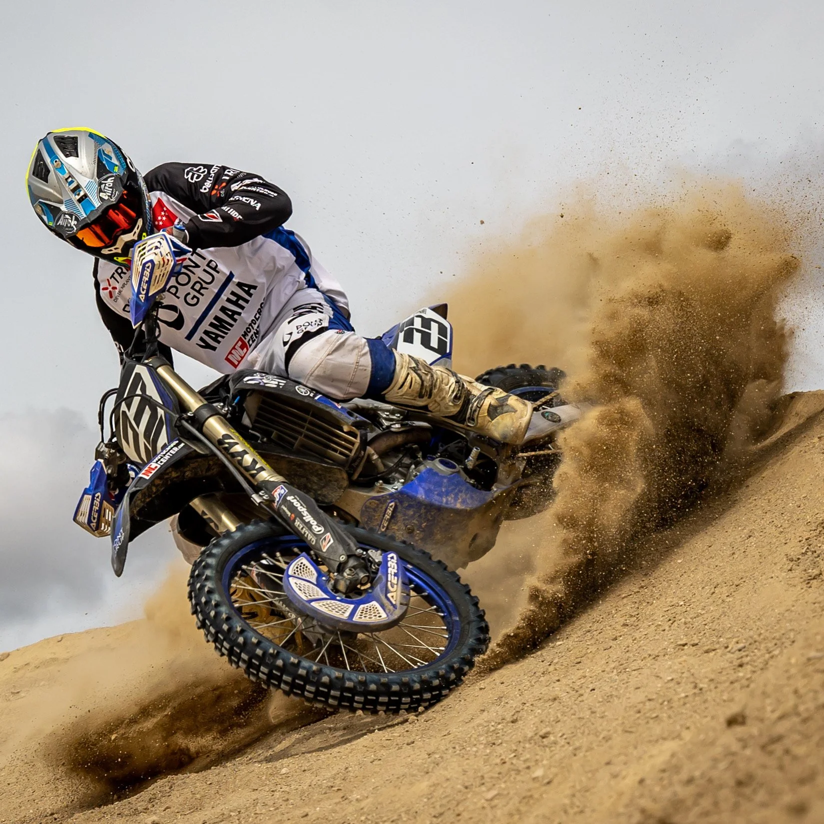 Un motociclista en acción en un desierto, levantando arena mientras toma una curva en una carrera de rally.