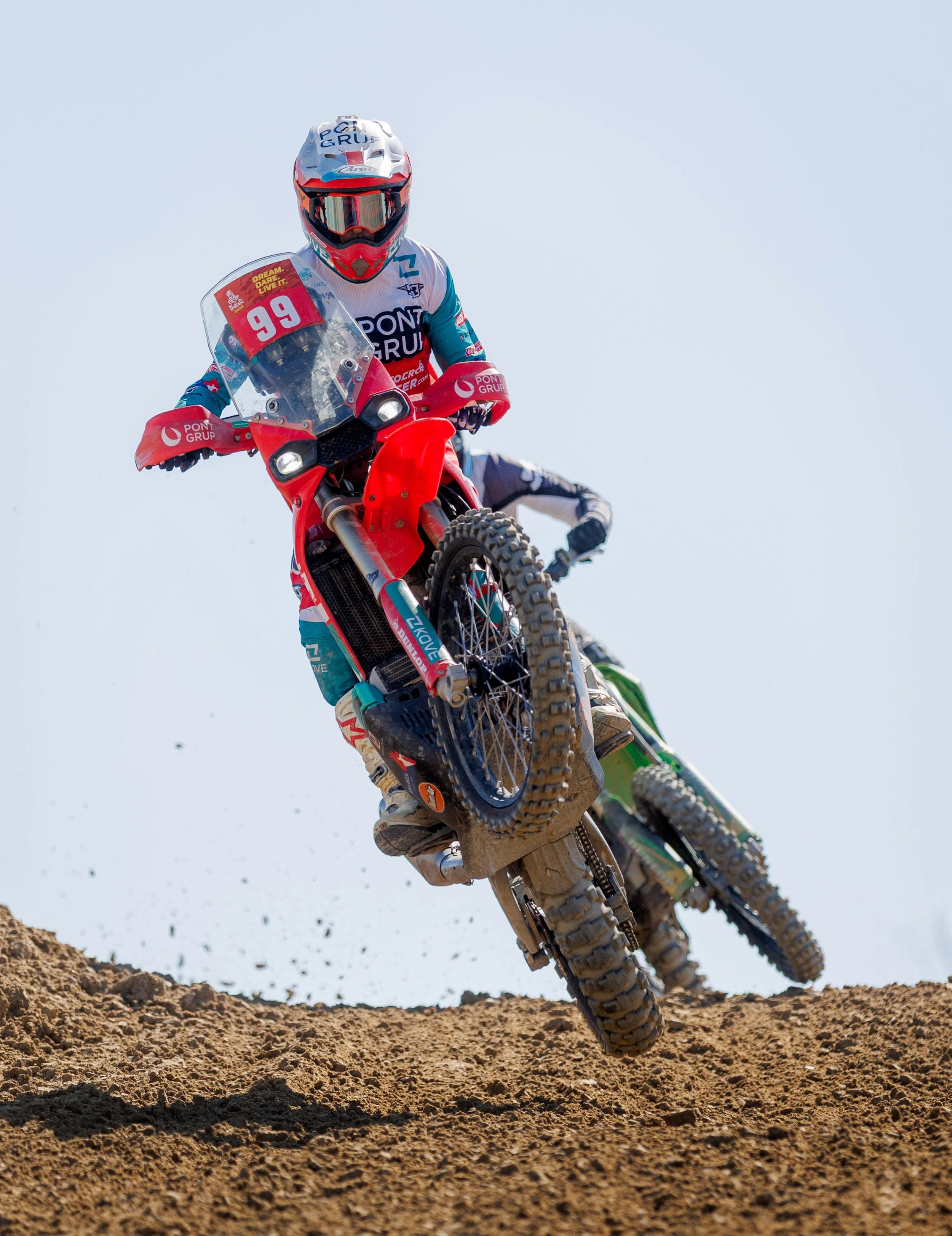 Dos motociclistas de motocross en una pista de tierra, con uno en primer plano levantado en el aire y el otro detrás rodas.