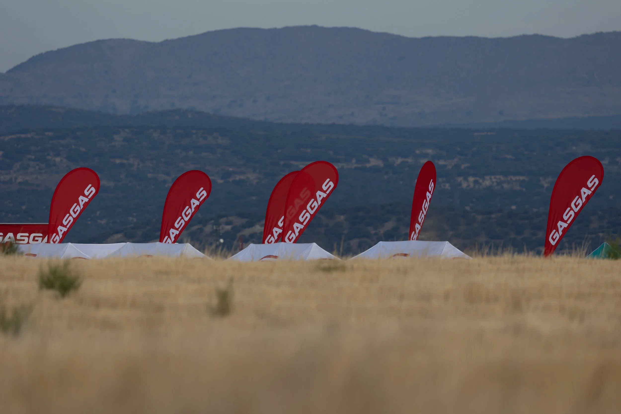 Vallas rojas con la palabra GASGAS en un campo con vegetación y montañas al fondo.