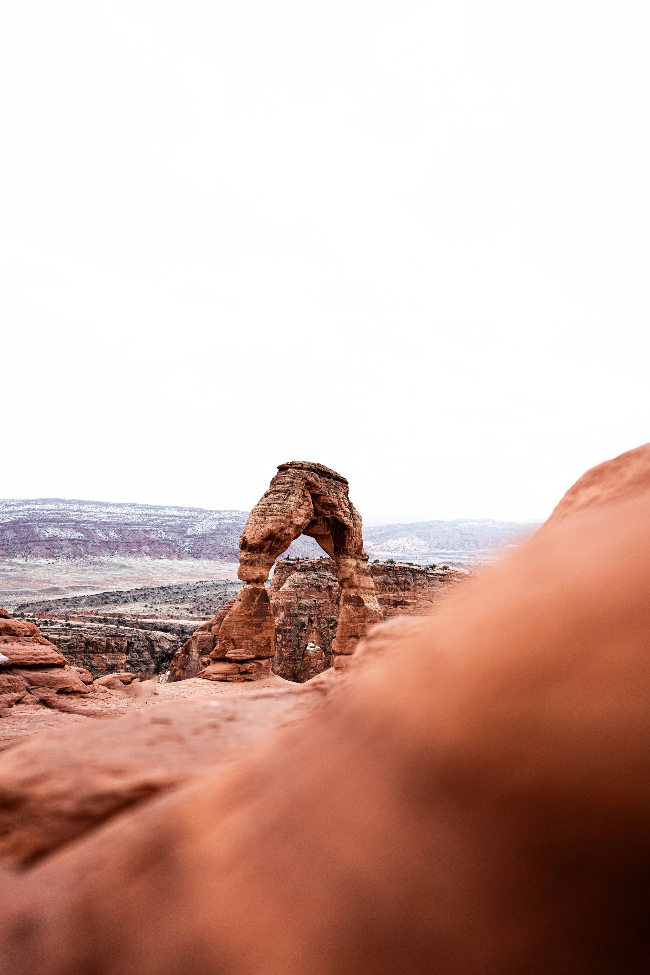 A famous natural rock formation called Delicate Arch in Arches National Park, Utah, with reddish sandstone and a cloudy sky.