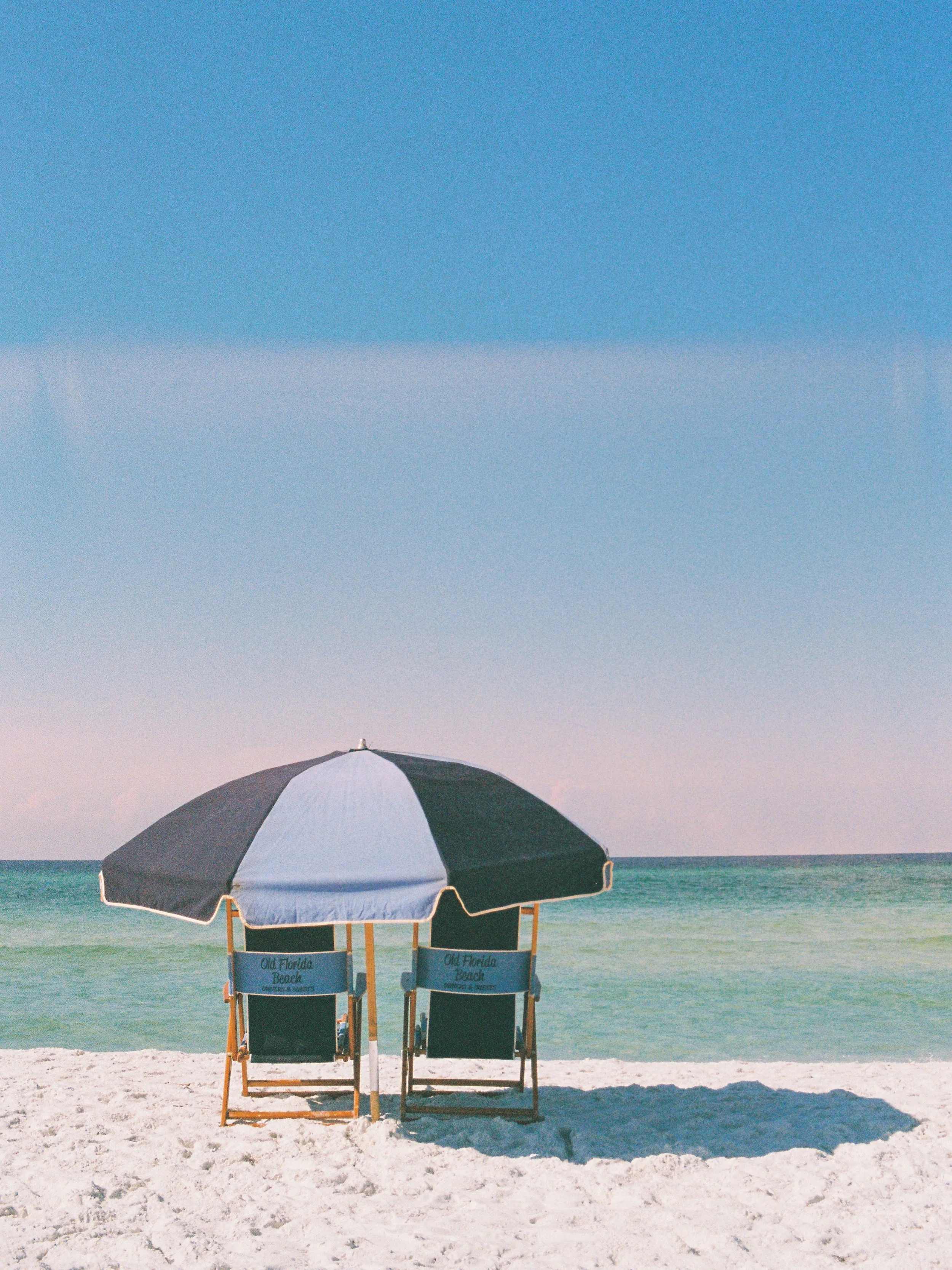 Two beach chairs under a large black and white umbrella on a sandy beach with ocean waves and clear blue sky in the background.