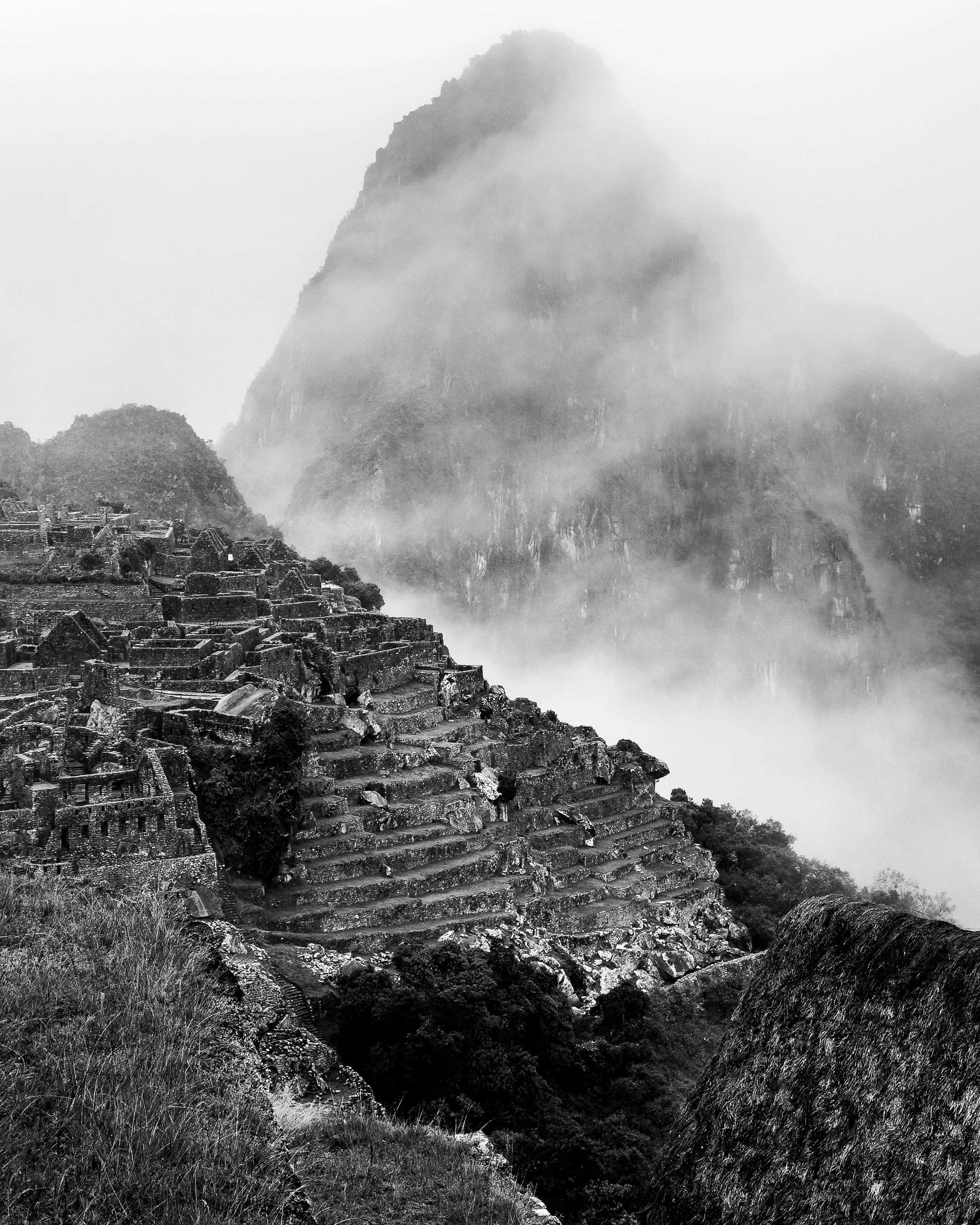 Ancient stone ruins in a misty mountain landscape, with steep terraces and fog-covered peaks in the background.