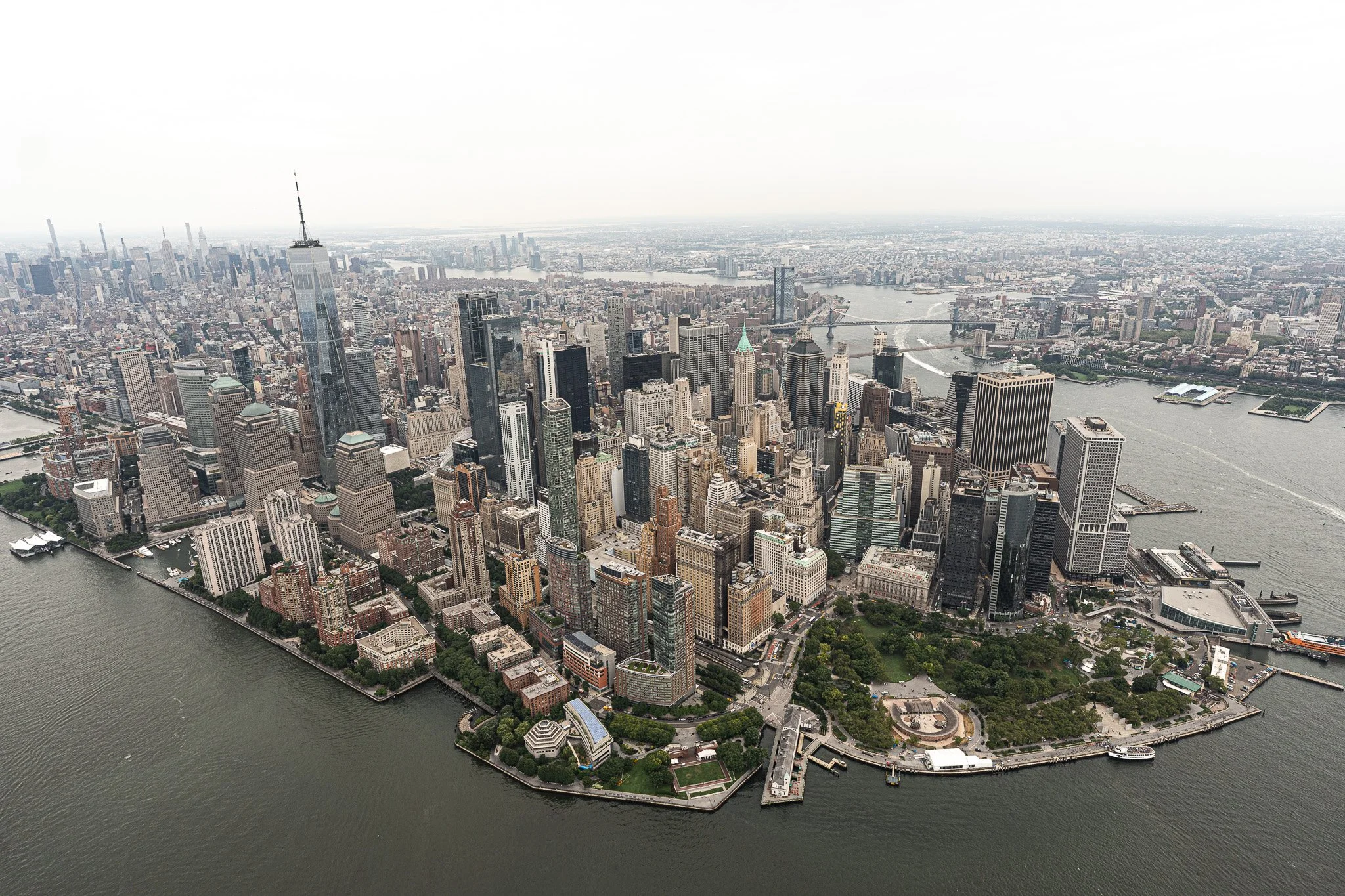 Aerial view of Manhattan skyline with tall skyscrapers and Manhattan Island surrounded by water, including the Hudson River and East River.