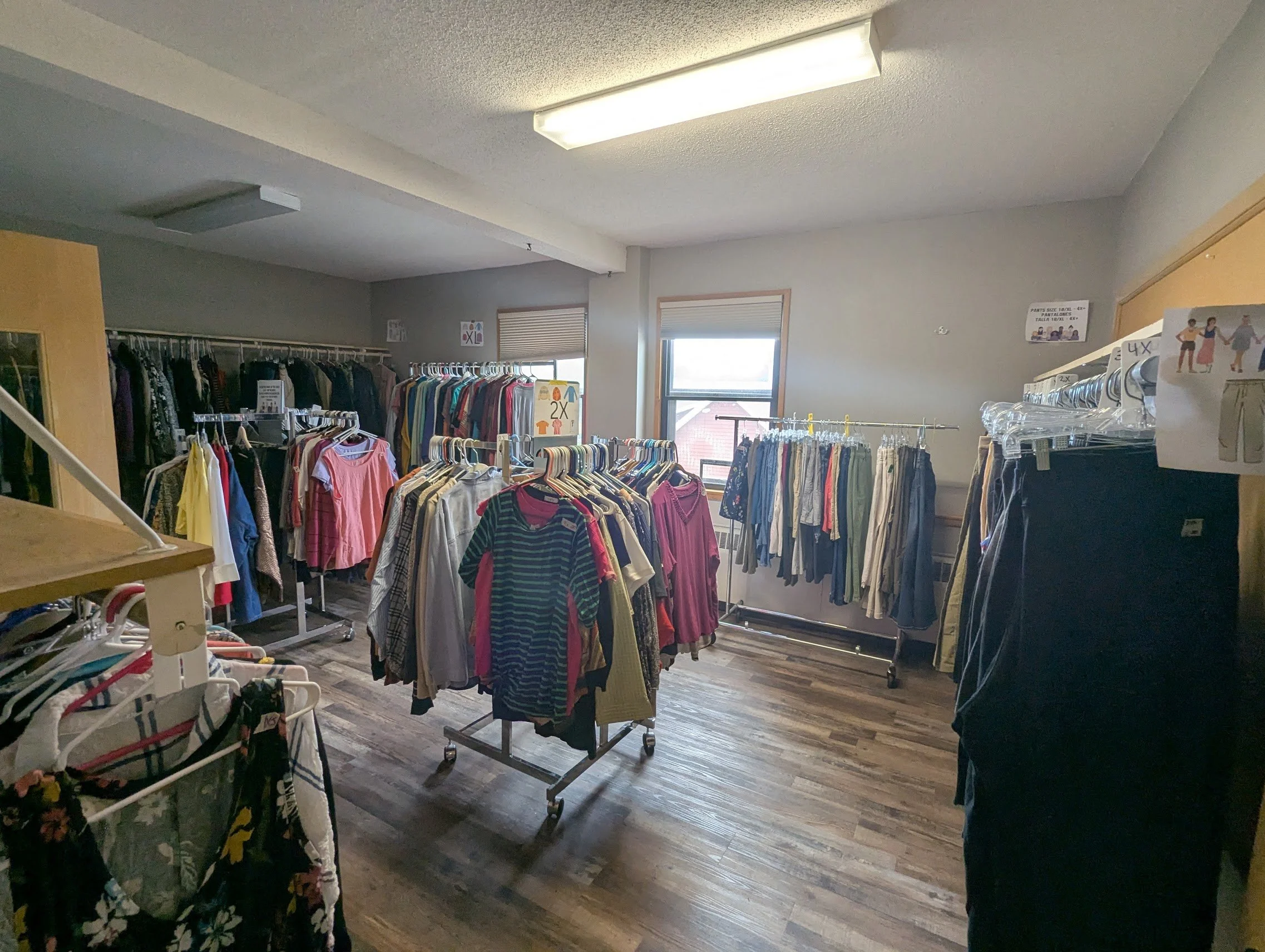Inside a thrift store or clothing boutique with racks of clothes, some on wheels, and a person partially visible on the right side.