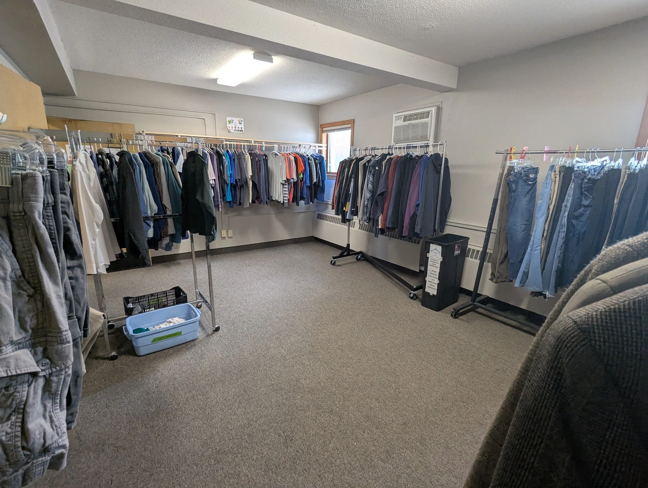 Clothing racks inside a room with beige carpet, filled with various shirts, jackets, and pants.