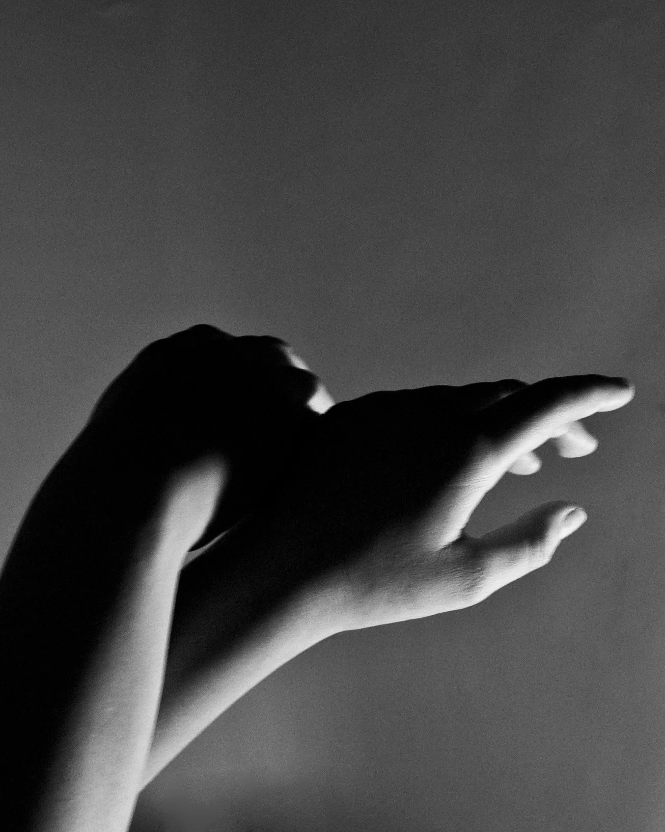 A black and white photo of a person's hand reaching out with fingers extended towards the right, against a plain background.