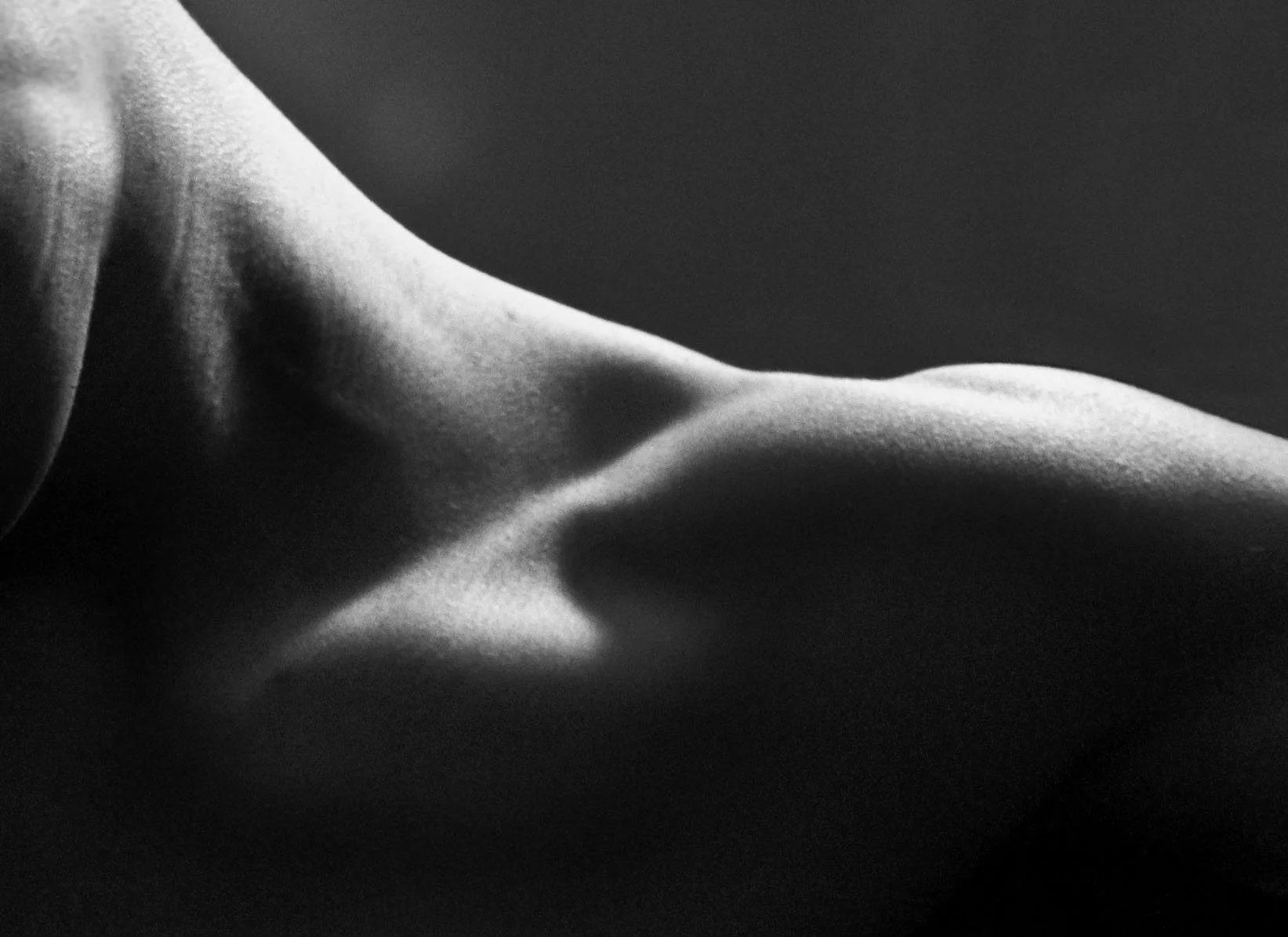 Close-up black and white photo of a human body part, possibly a shoulder or arm, with smooth skin and soft lighting.