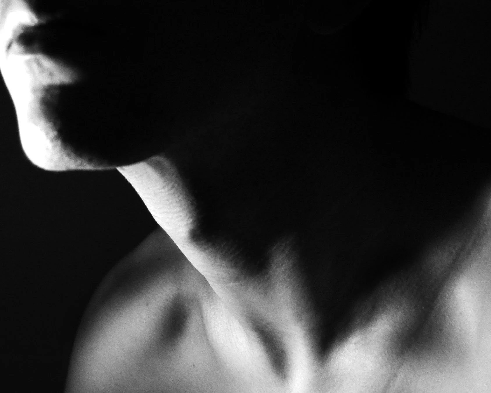 Close-up of a person's neck and lower face in black and white, with shadows emphasizing contours.