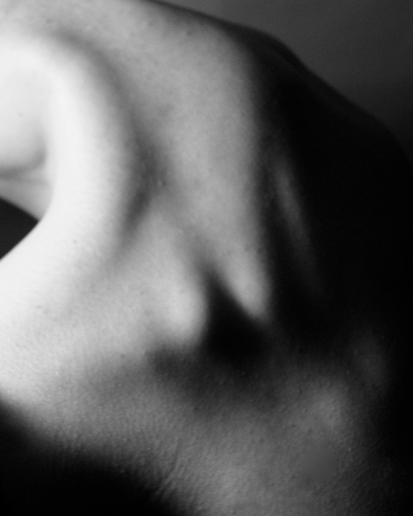 Close-up black and white photograph of a person's neck and shoulder, focusing on the skin texture and contours.
