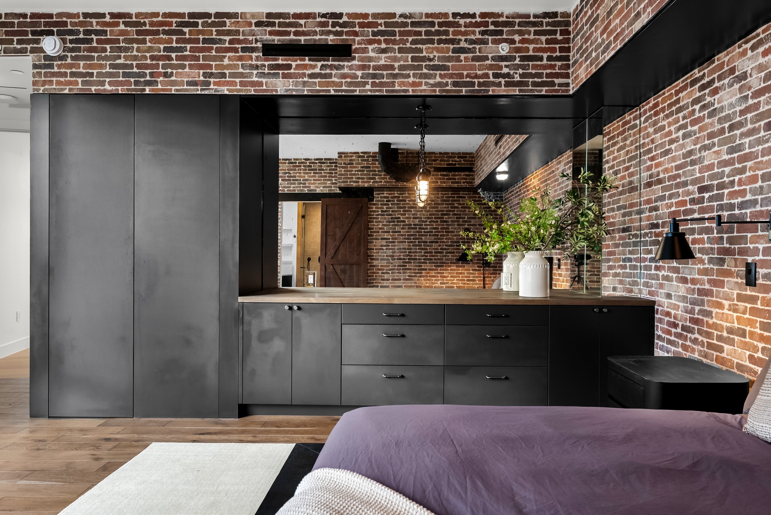 Custom primary bedroom with exposed brick walls, built-in storage, black cabinetry, and oversized mirror in a Downtown Austin penthouse