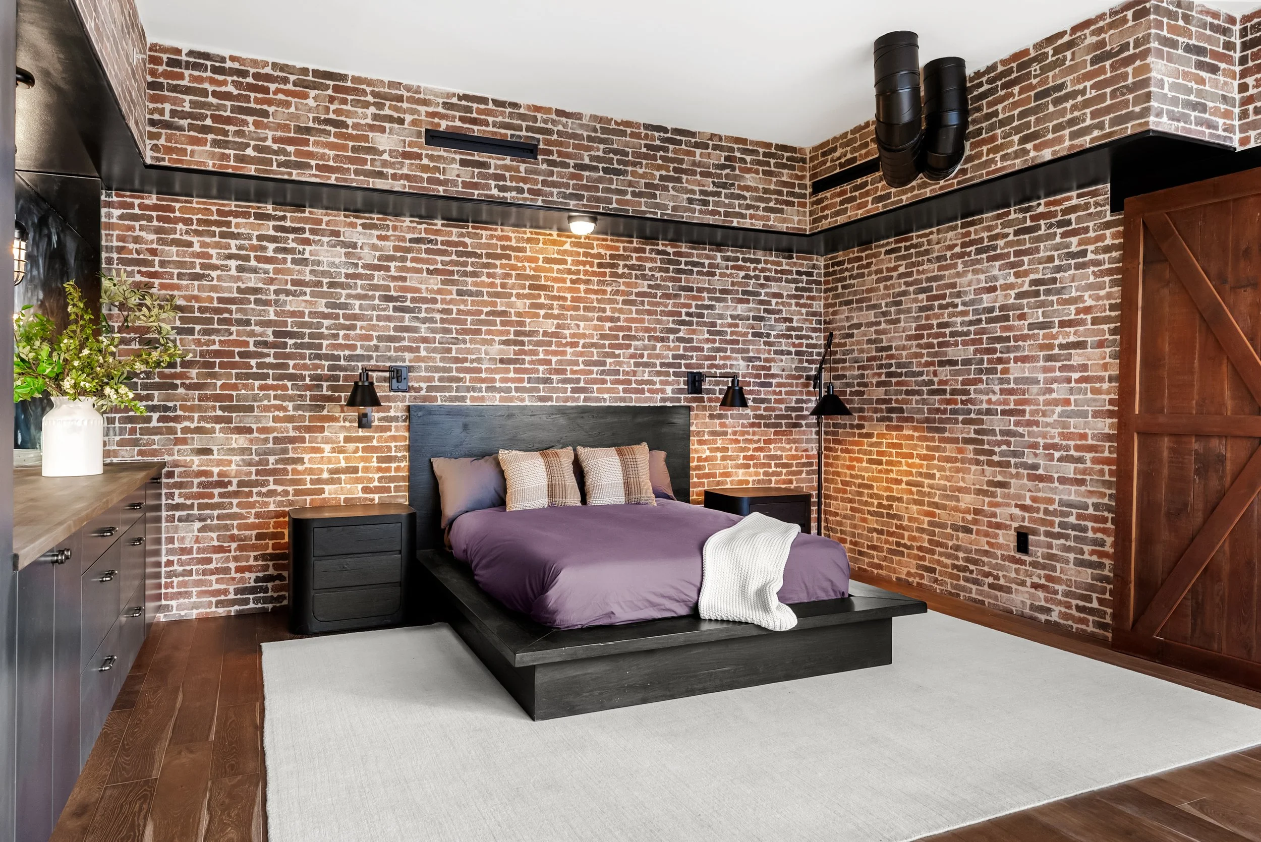 Custom bedroom featuring exposed brick walls, built-in black cabinetry, a custom platform bed, and barn door detailing