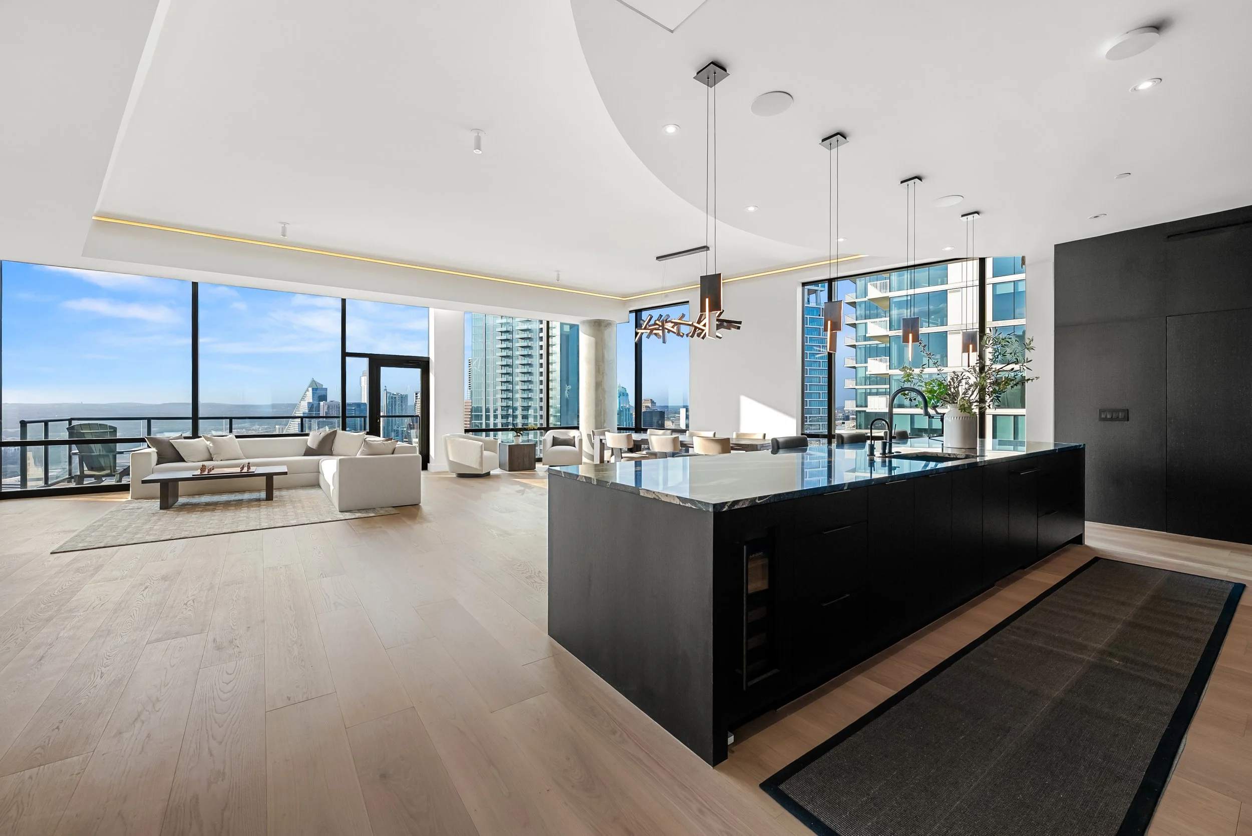 Open-concept luxury penthouse kitchen with custom black cabinetry, large stone island, and panoramic Downtown Austin views