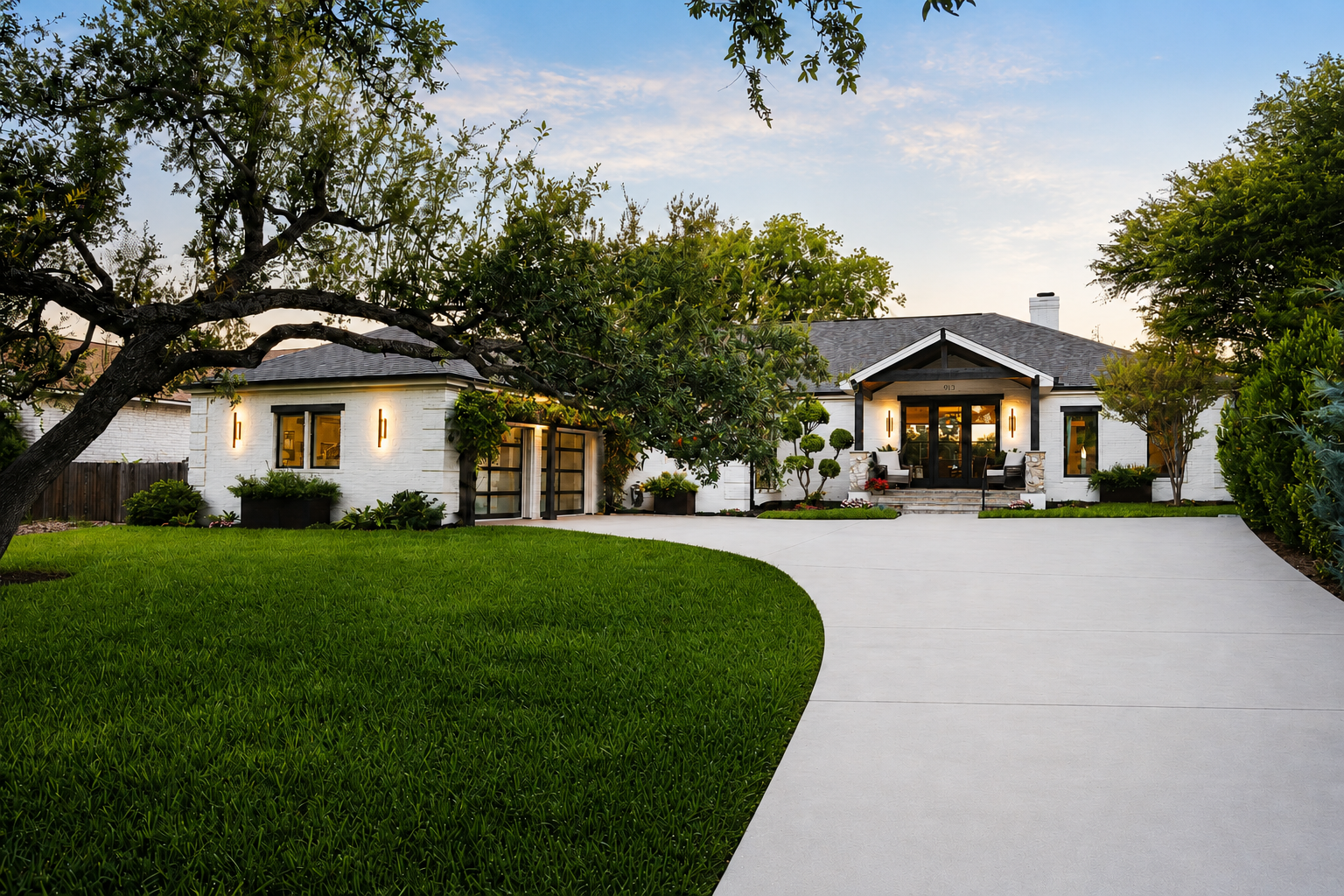 Custom home in Old Lakeway featuring white brick exterior, landscaped grounds, modern garage doors, and a wide concrete driveway