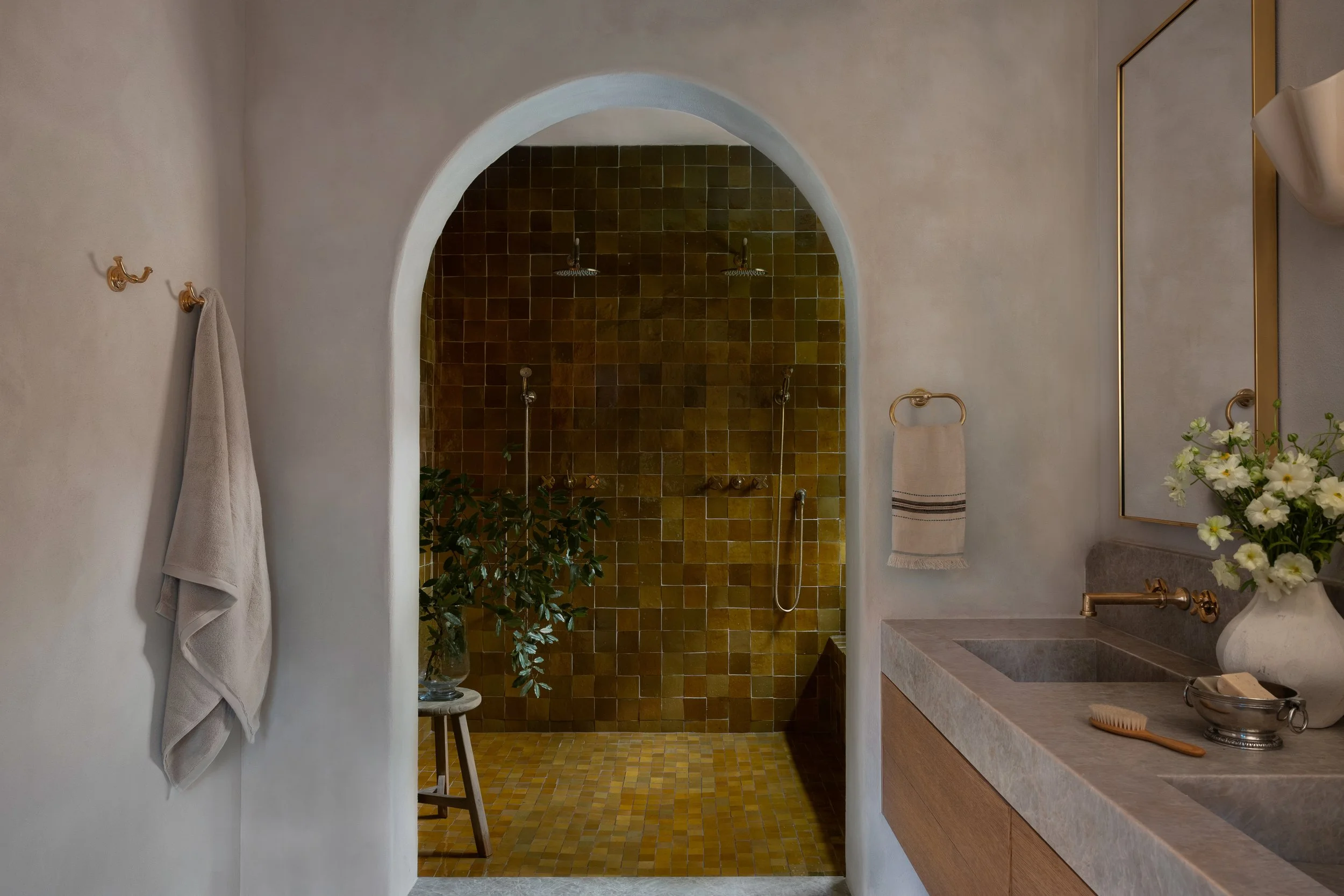 Luxury walk-in shower with warm olive tile, dual showerheads, handheld fixtures, and arched entry in a Travis Heights bathroom renovation
