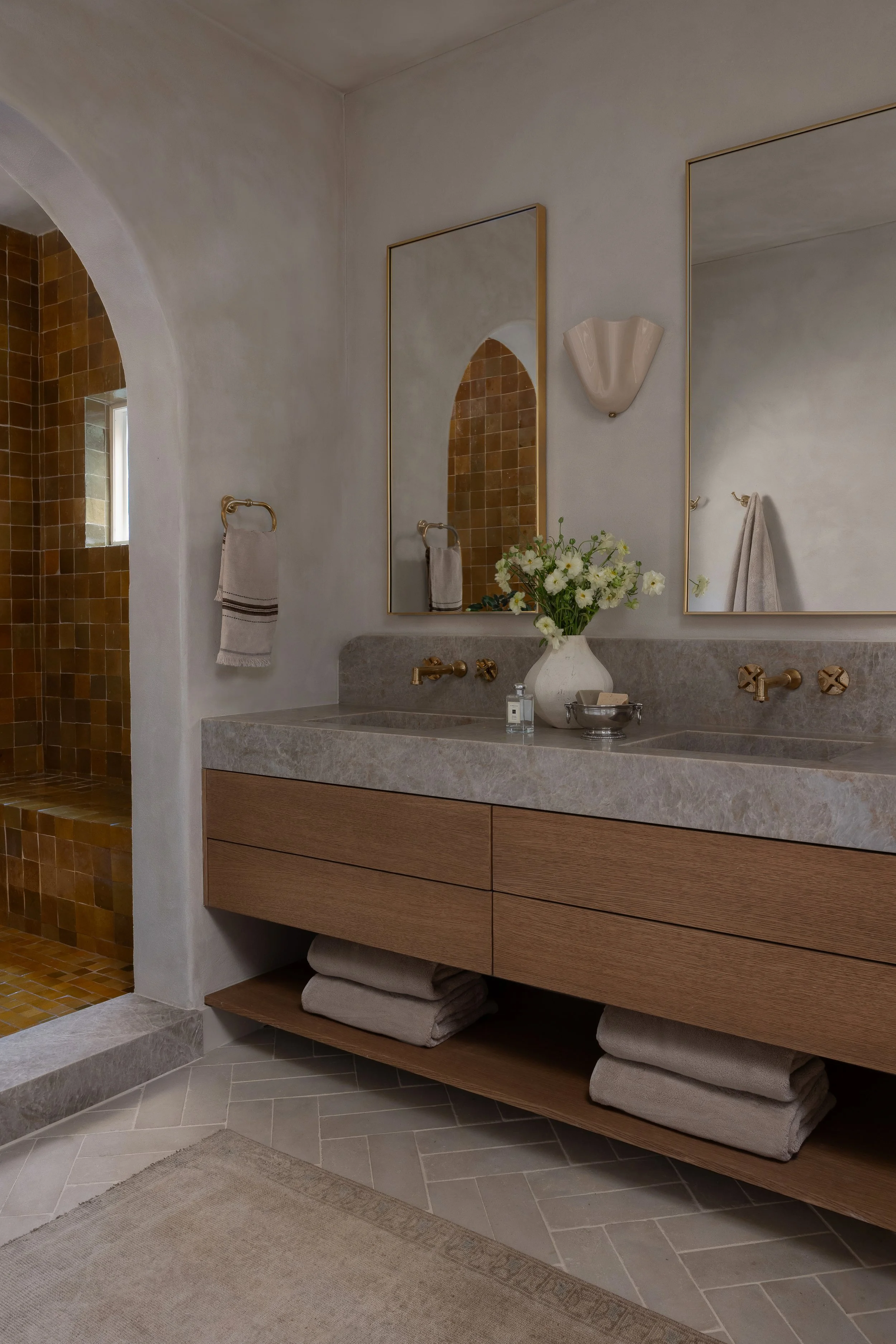 Custom oak double vanity with stone countertop, brass fixtures, framed mirrors, and open towel storage in a Travis Heights primary bathroom remodel